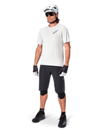 Ciclista MTB che indossa la maglia a maniche corte Alpinestars A-Aria Astar in White Dove, abbinata a pantaloncini da mountain bike neri, casco bianco e ginocchiere nere, con un piccolo logo nero sul petto, equipaggiamento tecnico coordinato per performance sui sentieri