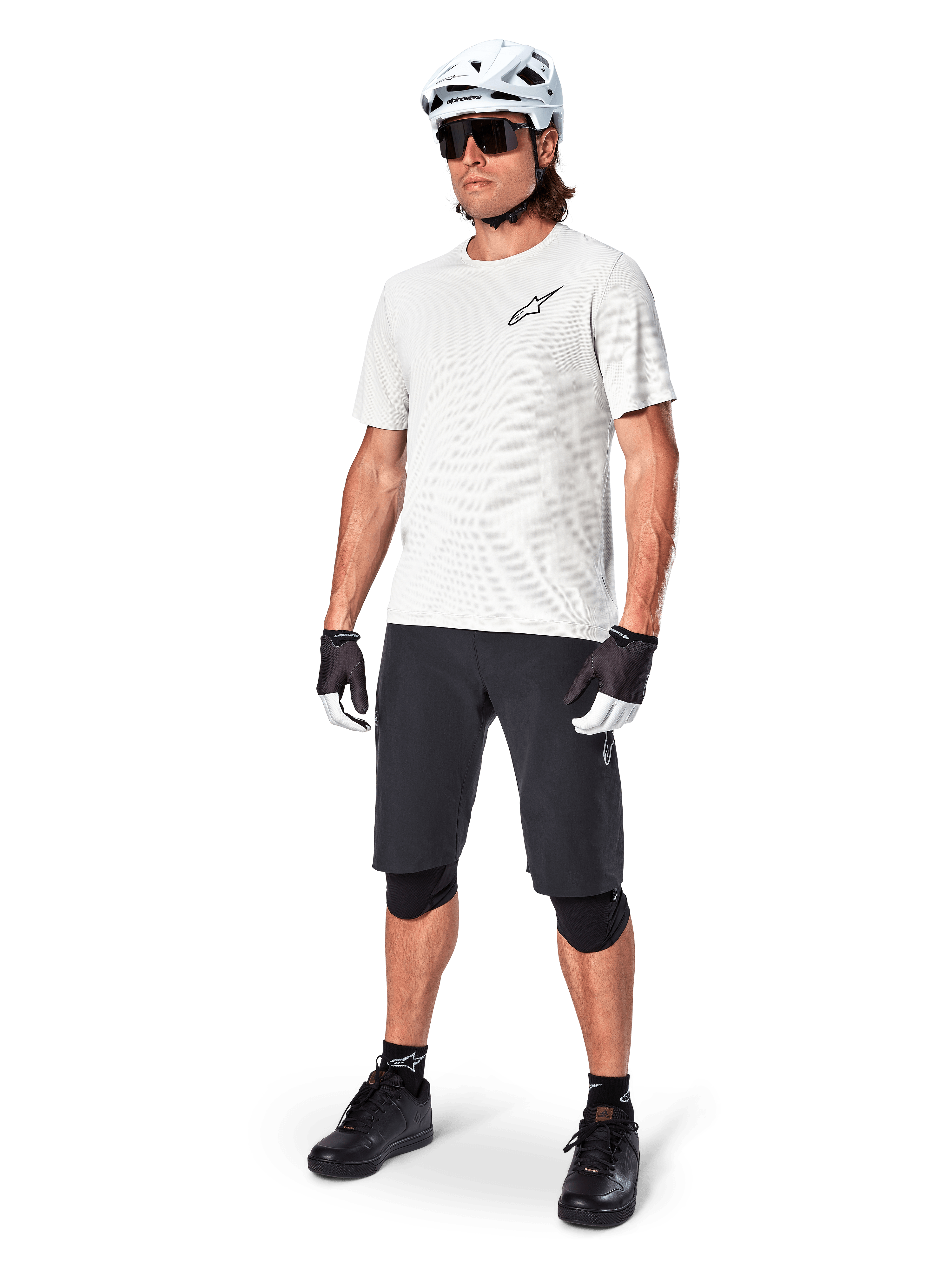Ciclista MTB che indossa la maglia a maniche corte Alpinestars A-Aria Astar in White Dove, abbinata a pantaloncini da mountain bike neri, casco bianco e ginocchiere nere, con un piccolo logo nero sul petto, equipaggiamento tecnico coordinato per performance sui sentieri