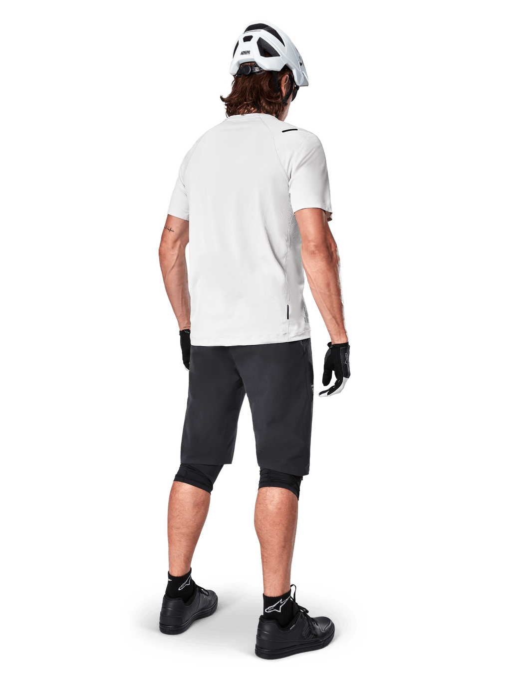 Ciclista che indossa la maglia a maniche corte Alpinestars A-Aria Astar in White Dove, vista posteriore, abbinata a pantaloncini da MTB neri, ginocchiere e casco bianco, equipaggiamento leggero e traspirante per mountain bike fuoristrada