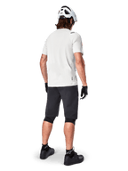 Ciclista che indossa la maglia a maniche corte Alpinestars A-Aria Astar in White Dove, vista posteriore, abbinata a pantaloncini da MTB neri, ginocchiere e casco bianco, equipaggiamento leggero e traspirante per mountain bike fuoristrada