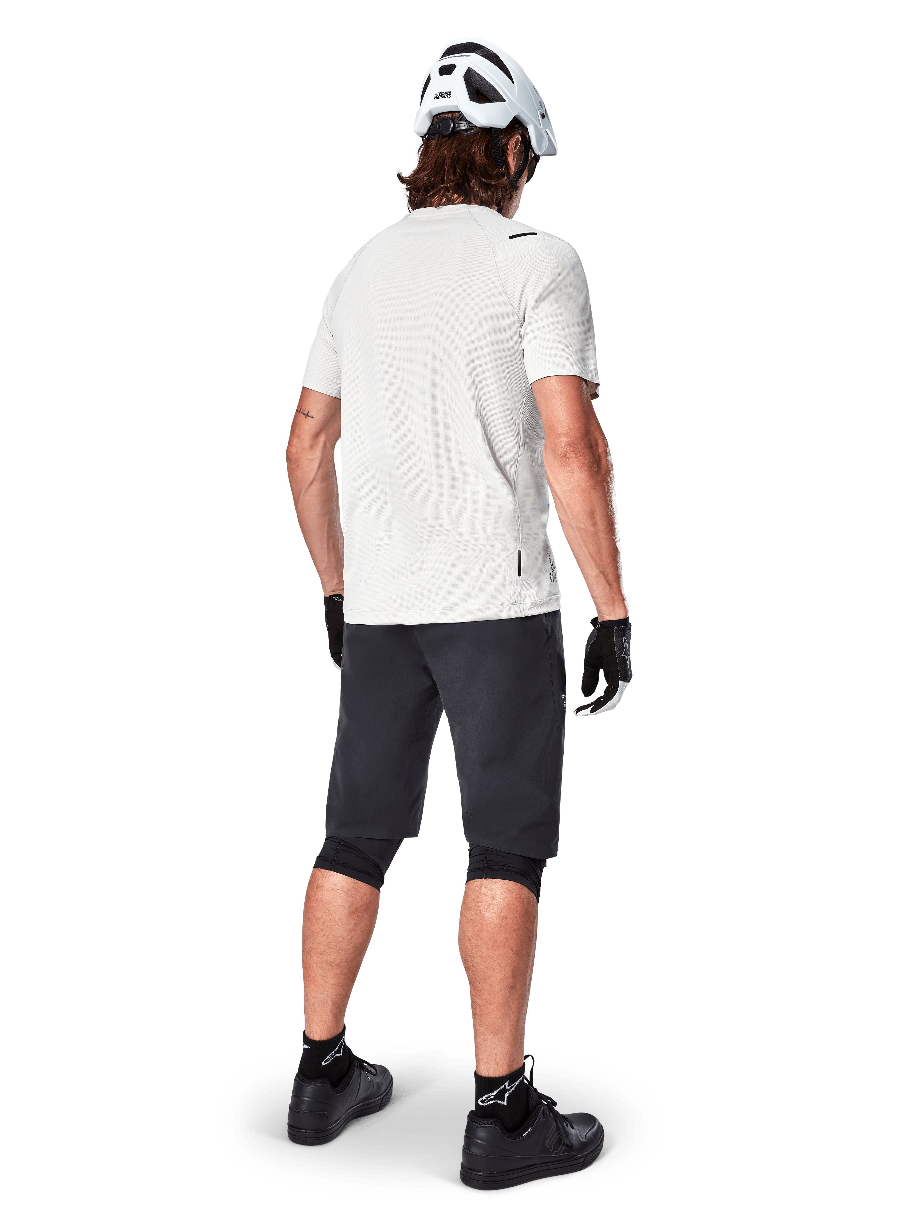 Ciclista che indossa la maglia a maniche corte Alpinestars A-Aria Astar in White Dove, vista posteriore, abbinata a pantaloncini da MTB neri, ginocchiere e casco bianco, equipaggiamento leggero e traspirante per mountain bike fuoristrada