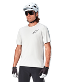 Alpinestars Maglia A-Aria Astar a maniche corte, White Dove, indossata da un ciclista con casco bianco e occhiali da sole scuri, con un piccolo logo a stella nero sul petto, abbigliamento performante traspirante per mountain bike
