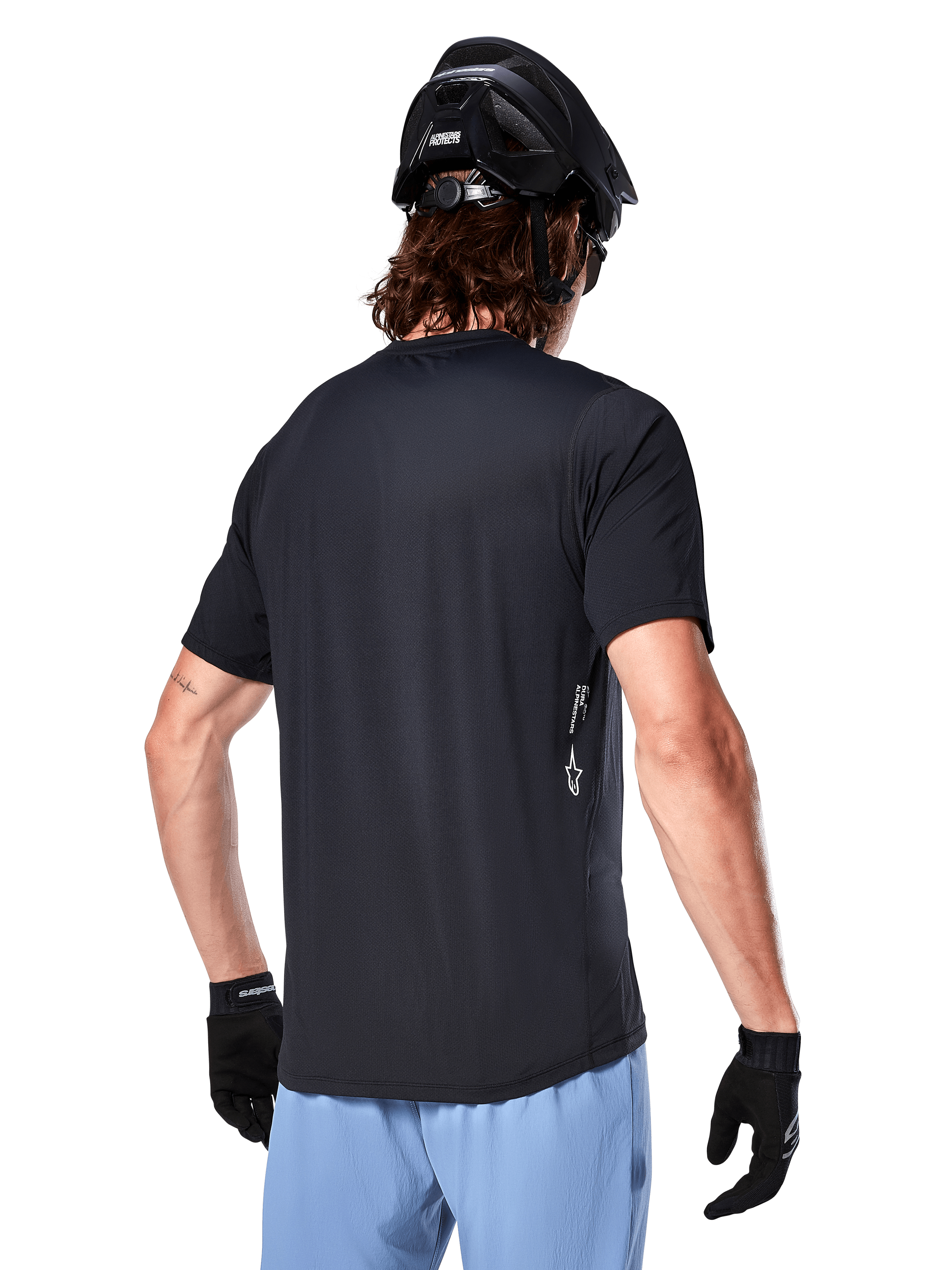 Alpinestars A-Dura Oscar Jersey, maglia da ciclismo a maniche corte, nero, vista posteriore su ciclista, abbinata a pantaloncini azzurri e casco MTB nero, piccolo logo bianco sul lato, abbigliamento tecnico per mountain bike