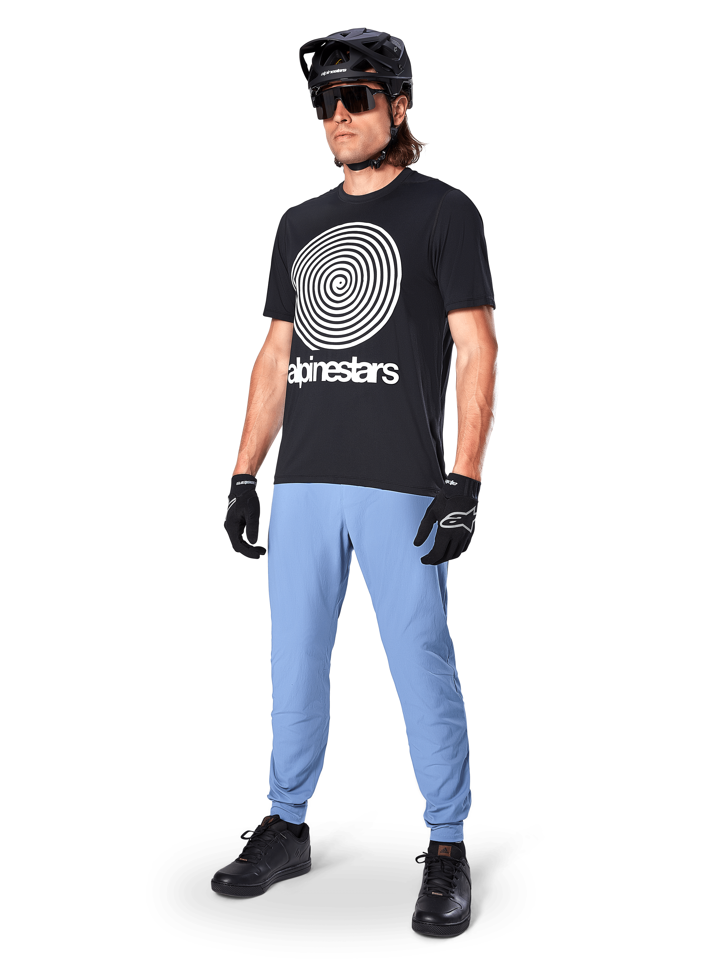 Maglia a maniche corte Alpinestars A-Dura Oscar, maglia da MTB nera con grande grafica a spirale heritage bianca, indossata da un rider con casco nero, occhiali da sole, guanti neri e pantaloni azzurri, abbigliamento tecnico da mountain bike