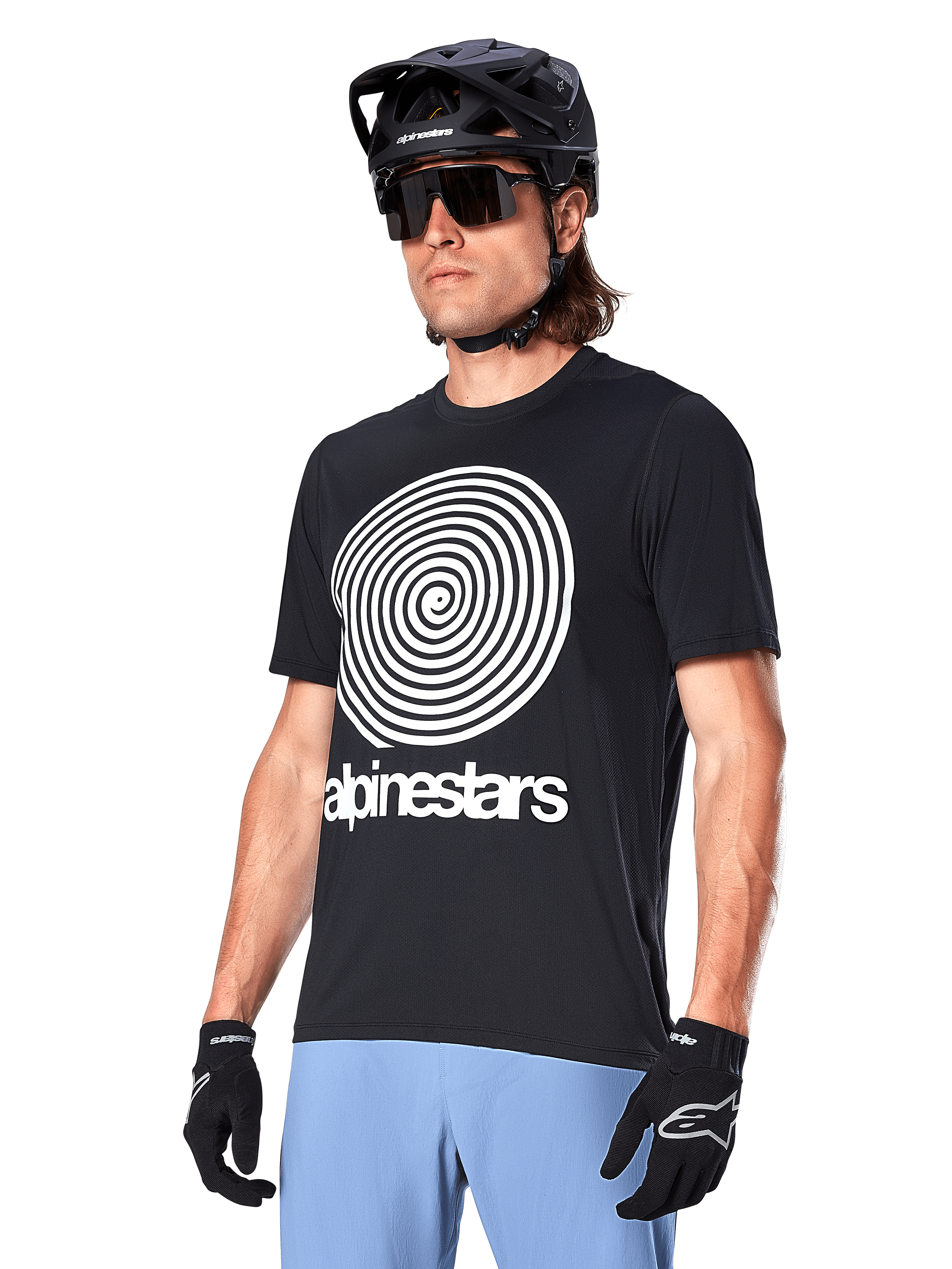 Alpinestars A-Dura Oscar Jersey - Manica Corta, nero, con grande grafica a spirale bianca e marchio Alpinestars sul petto, indossata da un ciclista con casco da MTB nero, occhiali da sole e pantaloni azzurri