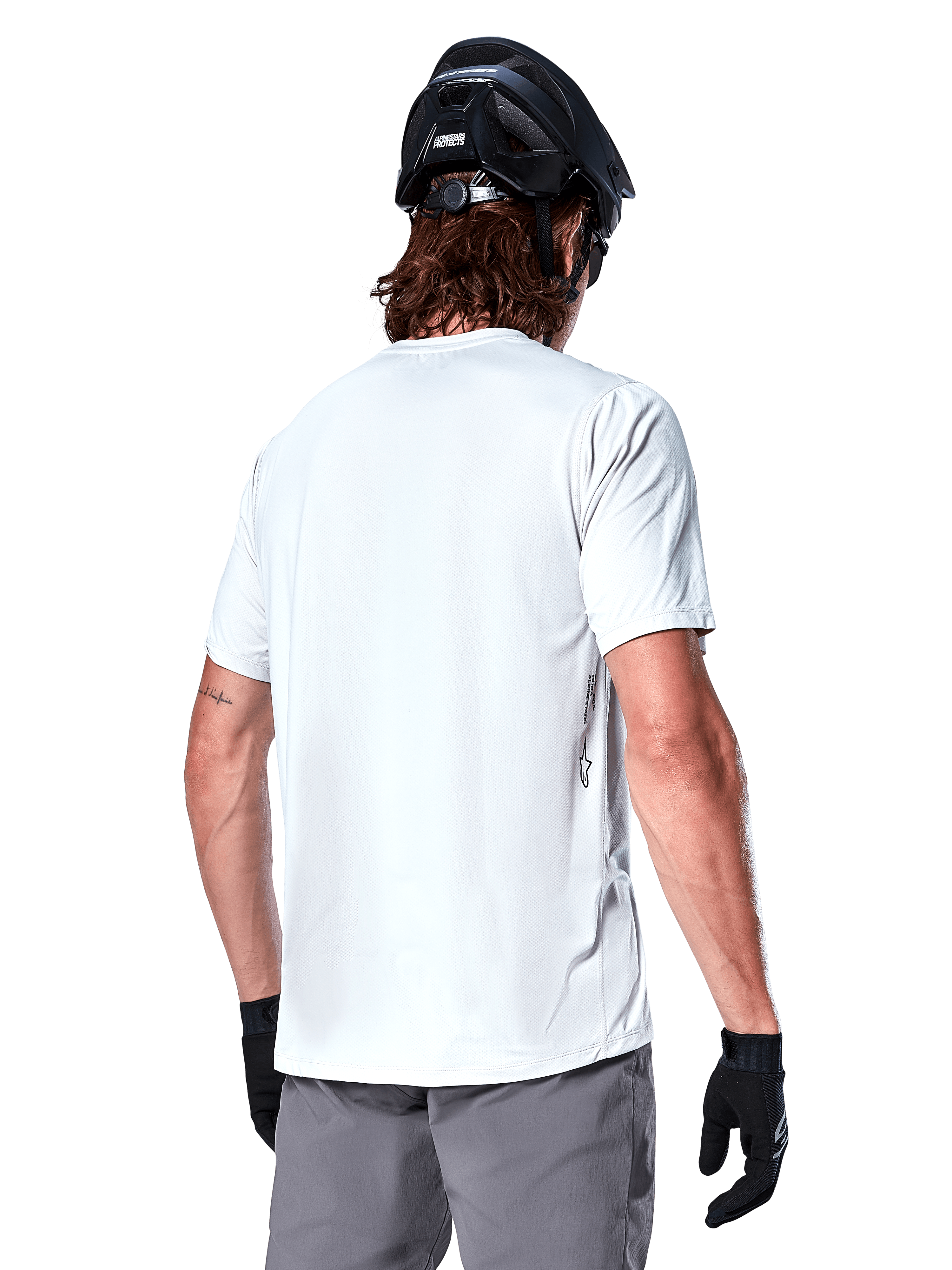 Alpinestars Maglia A-Dura Oscar, maglia MTB a maniche corte, White Dove, vista posteriore su un ciclista con casco da ciclismo nero, pantaloncini grigi e guanti neri, abbigliamento tecnico da ciclismo