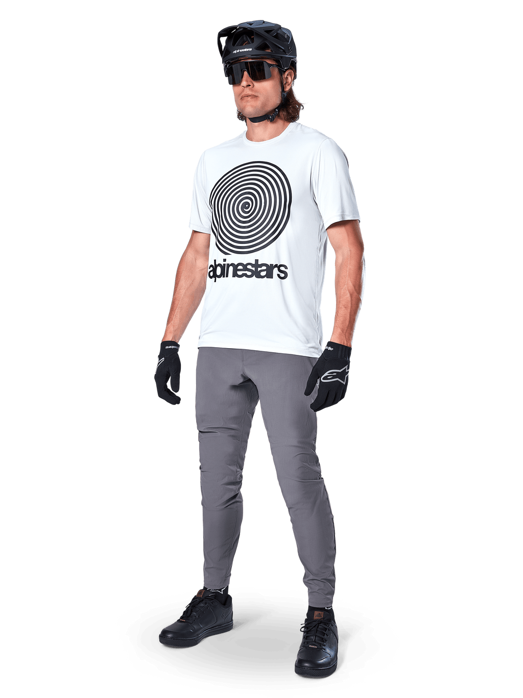 Alpinestars Maglia A-Dura Oscar a maniche corte, White Dove con grande grafica a spirale nera, indossata da un ciclista con pantaloni MTB grigi, casco nero e guanti, abbigliamento tecnico da ciclismo per guida off-road