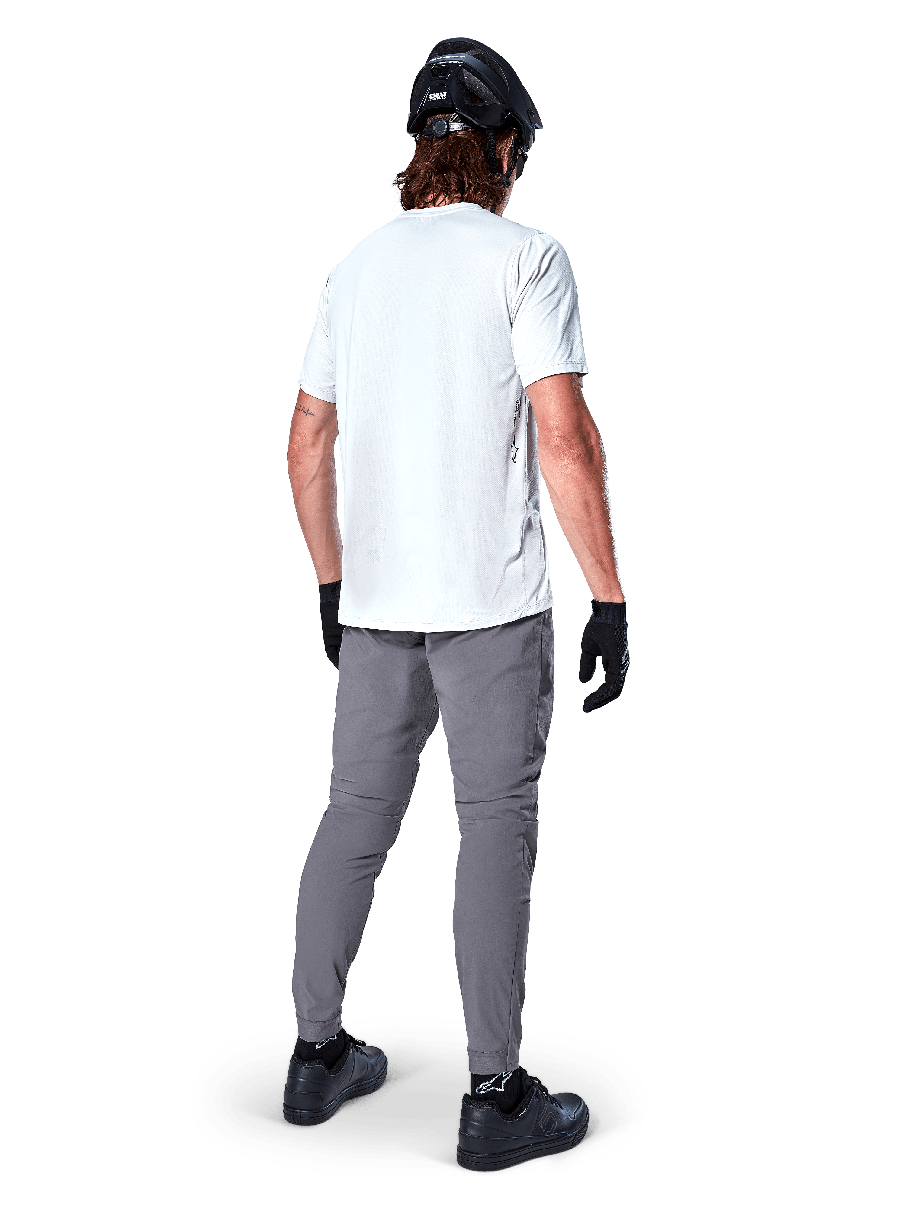 Maglia a maniche corte Alpinestars A-Dura Oscar in White Dove, vista posteriore indossata da un rider con pantaloni da ciclismo grigi, casco nero e guanti, abbigliamento tecnico da mountain bike per trail riding fuoristrada