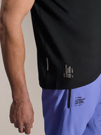 Alpinestars Maglia A-Aria Switch a maniche corte, maglia MTB nera, primo piano dell'orlo laterale con marchio bianco 'ONE GOAL. ONE VISION.', indossata con pantaloncini da ciclismo viola chiaro con loghi coordinati