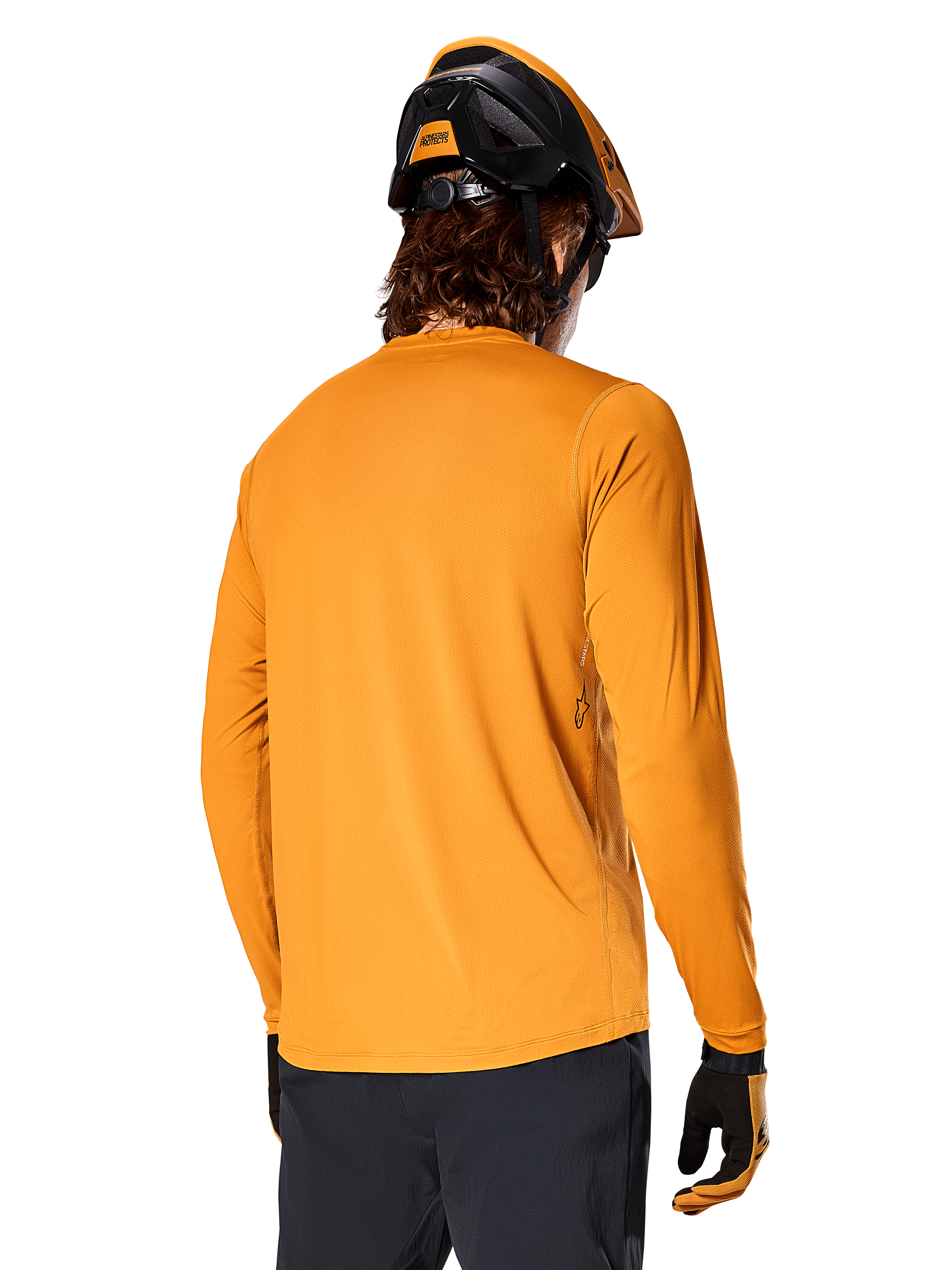 Maglia a maniche lunghe Alpinestars A-Dura Rocker, Dark Gold, vista posteriore del rider con casco da MTB nero e arancione, pantaloni scuri e guanti coordinati, abbigliamento da mountain bike casual ad alte prestazioni