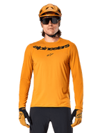 Maglia Alpinestars A-Dura Rocker a maniche lunghe in Dark Gold, con logo wordmark nero sul petto, indossata con casco e guanti coordinati color oro per prestazioni in mountain bike.