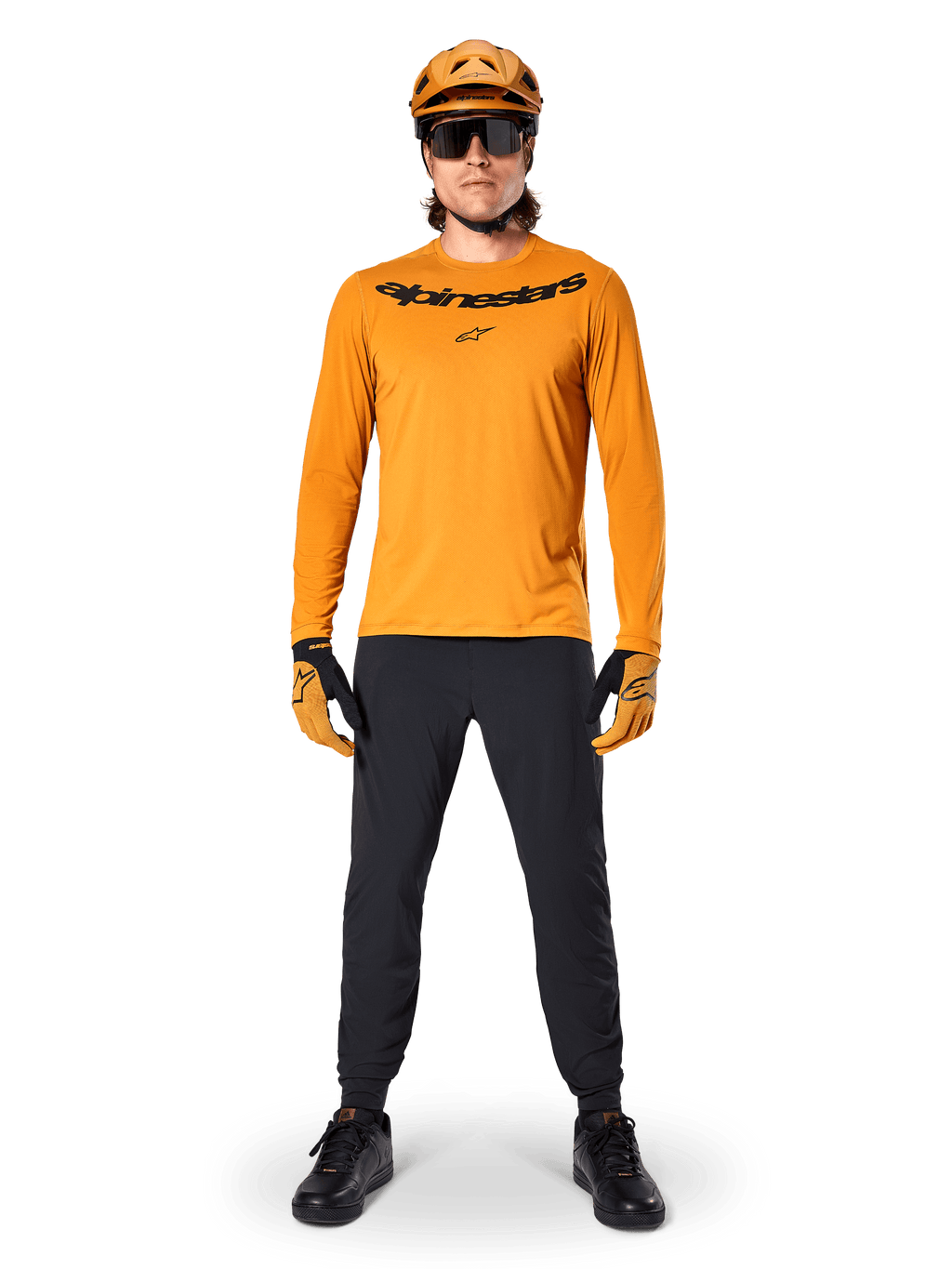 Alpinestars A-Dura Rocker Jersey - Long Sleeve in Dark Gold, con logo nero serigrafato sul petto, indossata con casco da MTB dorato coordinato, occhiali da sole e pantaloni neri, abbigliamento professionale da mountain bike