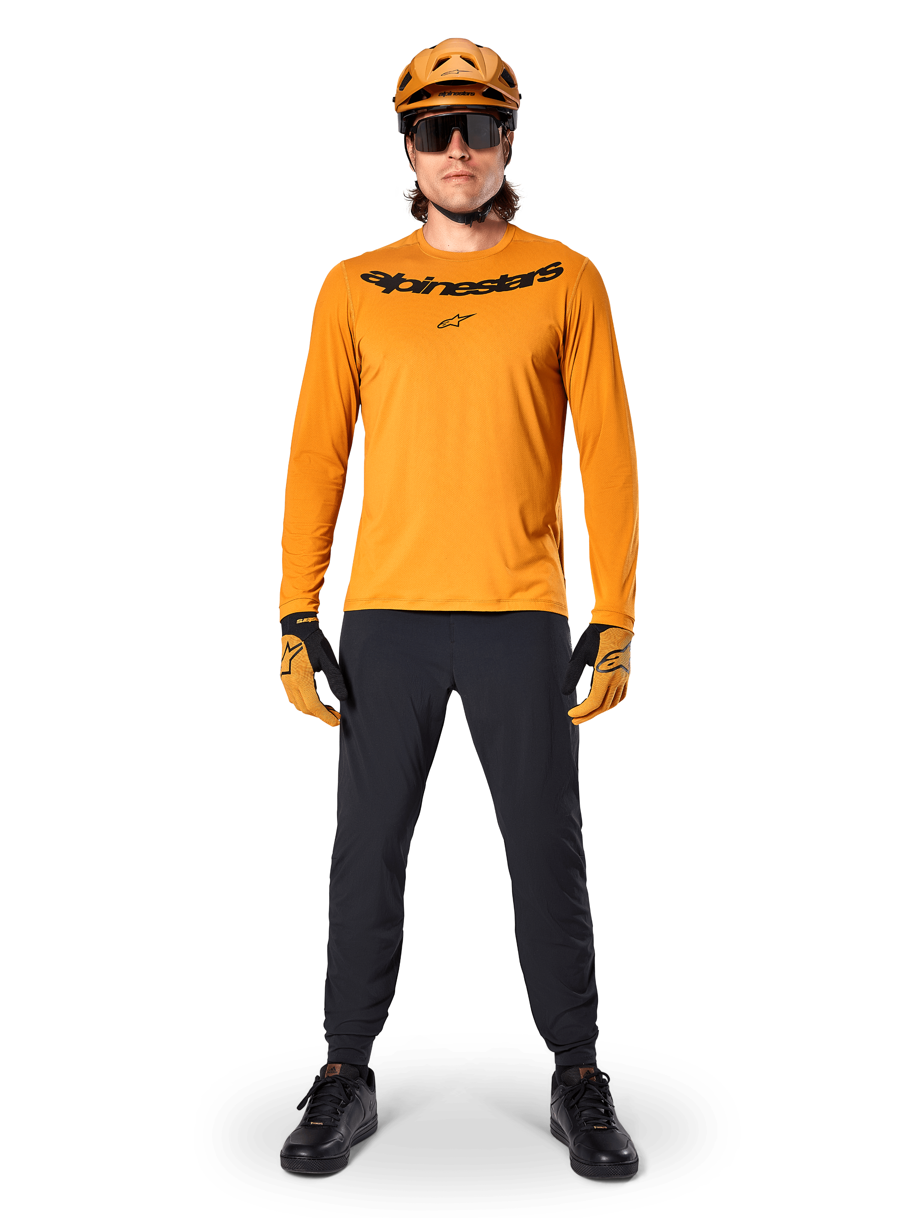 Alpinestars A-Dura Rocker Jersey - Long Sleeve in Dark Gold, con logo nero serigrafato sul petto, indossata con casco da MTB dorato coordinato, occhiali da sole e pantaloni neri, abbigliamento professionale da mountain bike