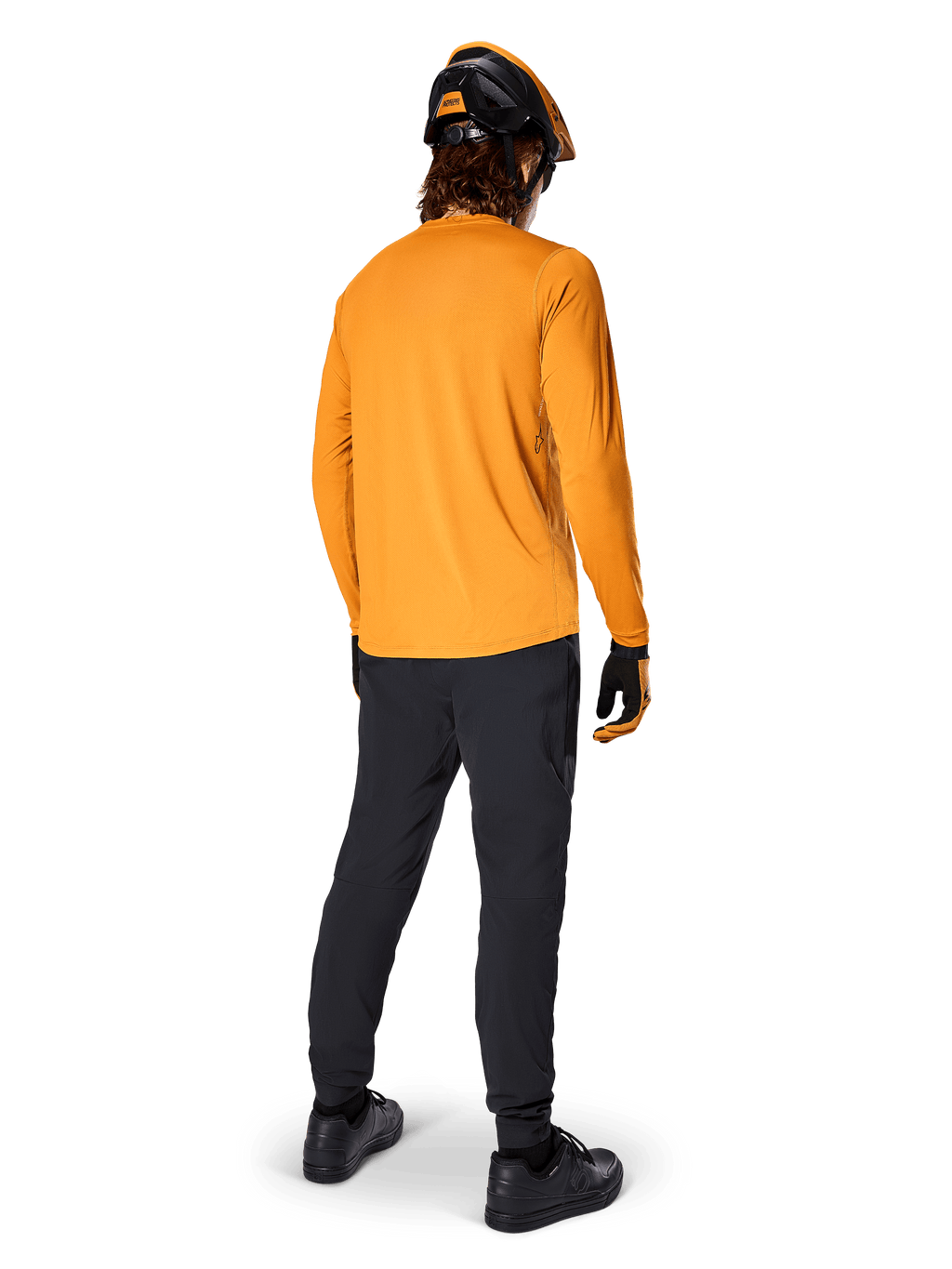 Ciclista di mountain bike visto da dietro che indossa la maglia a maniche lunghe Alpinestars A-Dura Rocker in Dark Gold, pantaloni neri, casco arancione e nero e scarpe nere, abbigliamento tecnico da MTB coordinato per trail riding