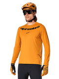 Alpinestars A-Dura Rocker Jersey a maniche lunghe, maglia da mountain bike MTB, Dark Gold, persona che indossa la maglia con casco e guanti coordinati, look sportivo coordinato con marchio Alpinestars sul petto