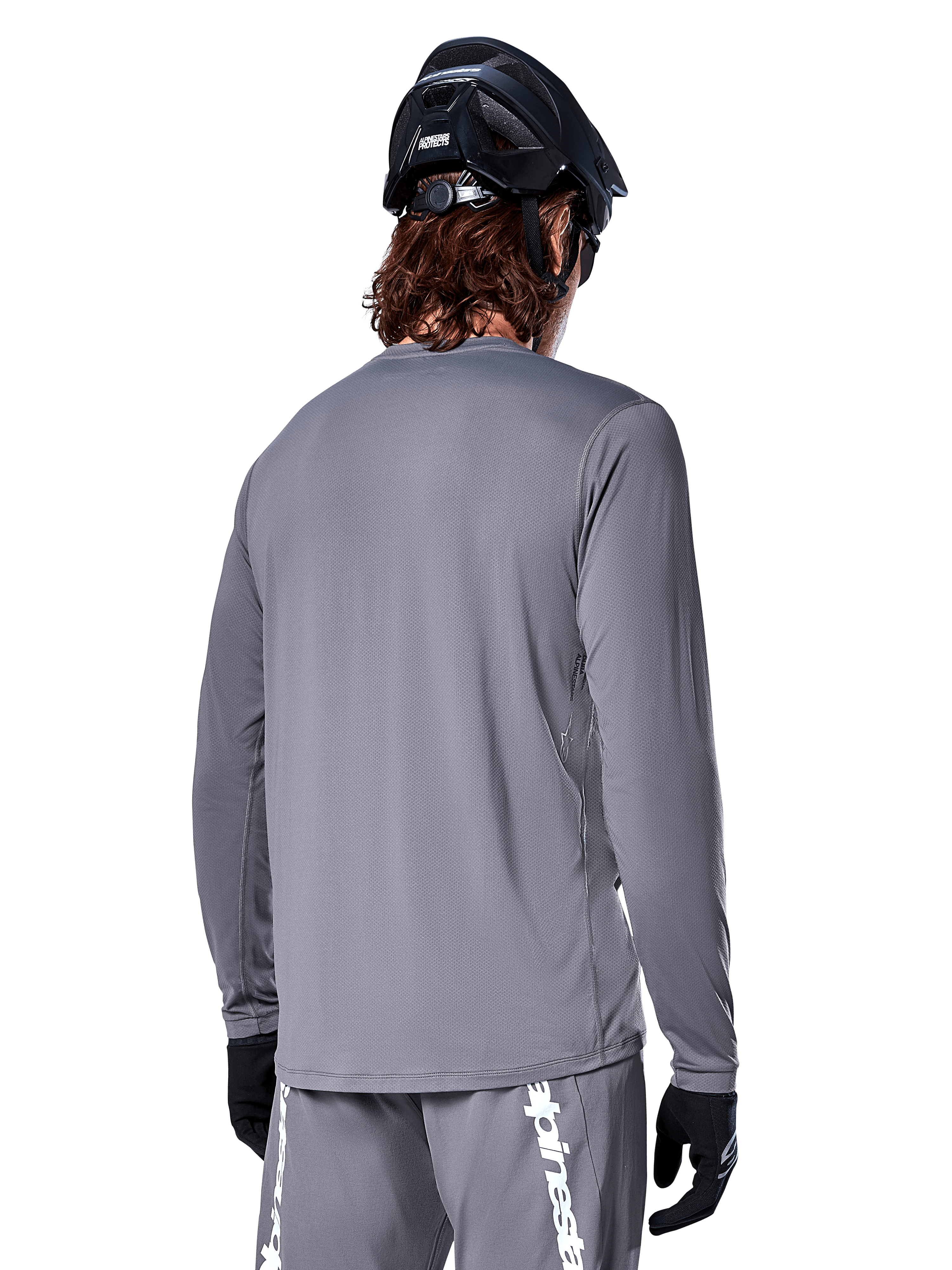 Maglia a maniche lunghe Alpinestars A-Dura Rocker in grigio scuro, vista posteriore di un ciclista di mountain bike, abbinata a pantaloncini grigi coordinati con branding bianco, casco da MTB nero e guanti neri, equipaggiamento professionale per ciclismo fuoristrada.
