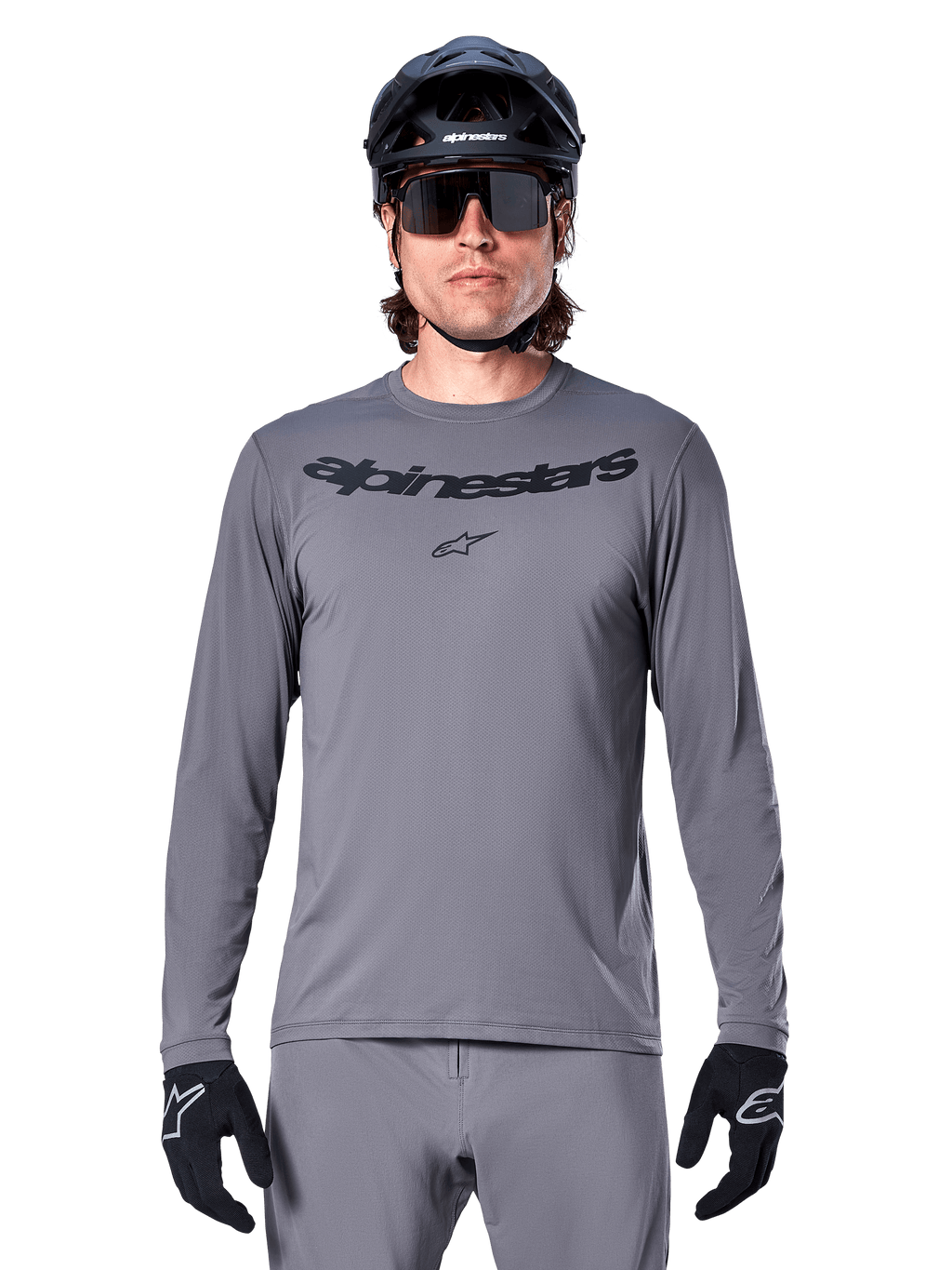 Ciclista che indossa la maglia Alpinestars A-Dura Rocker a maniche lunghe, maglia da MTB grigio scuro con logo nero sul petto, abbinata a pantaloni grigi, casco nero e guanti, progettata per il ciclismo fuoristrada