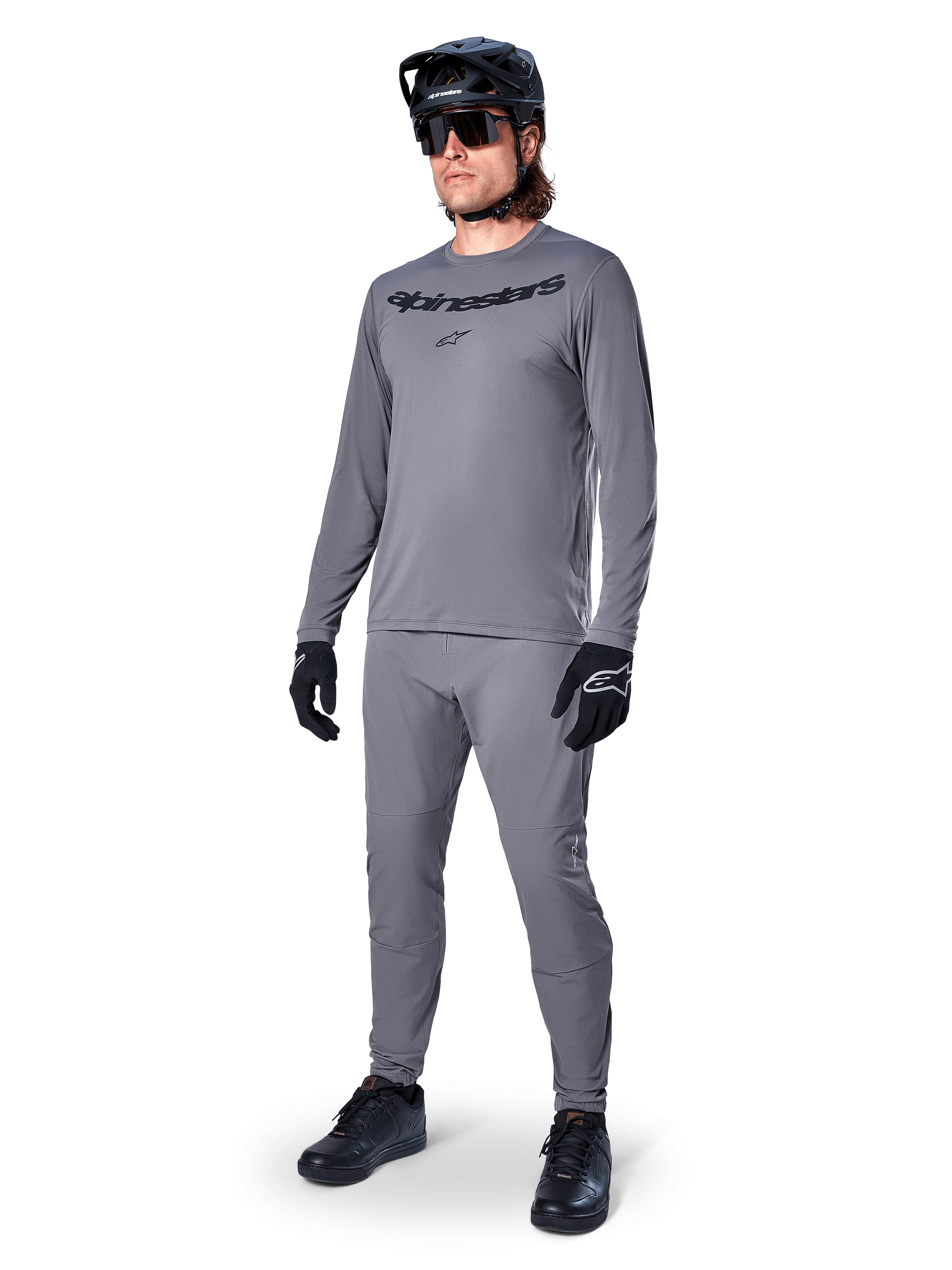 Alpinestars A-Dura Rocker Jersey - Maniche Lunghe, grigio scuro, indossata da un modello con pantaloni grigi coordinati, casco da mountain bike nero, occhiali da sole e guanti, stile casual MTB per la guida fuoristrada