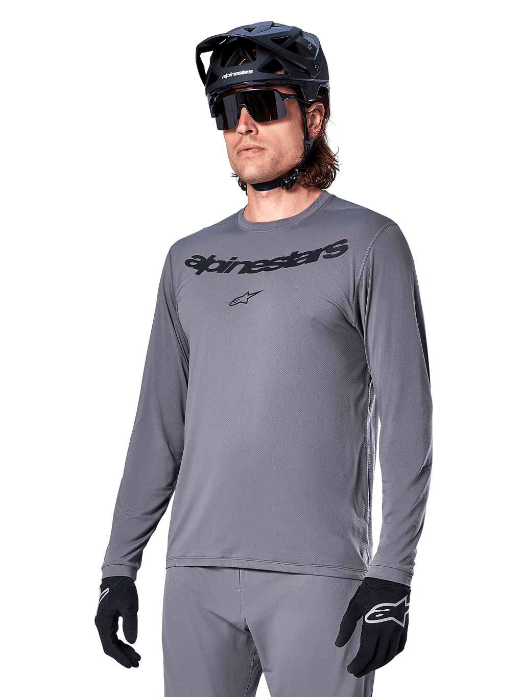 Alpinestars A-Dura Rocker Jersey a maniche lunghe, maglia da mountain bike grigia, indossata con casco e guanti neri, con scritta nera sul petto, abbigliamento sportivo da ciclismo per il fuoristrada, sfondo neutro