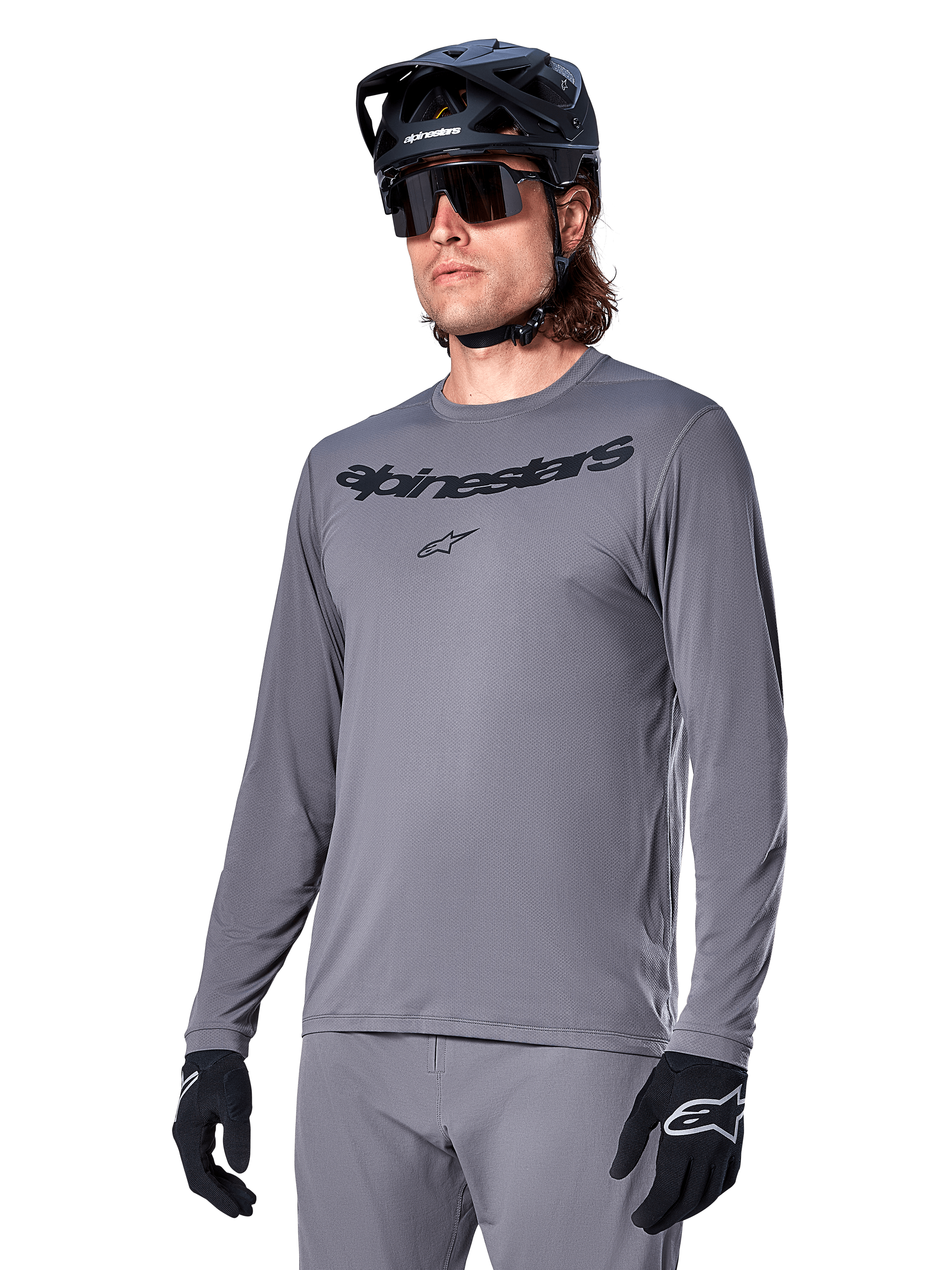 Alpinestars A-Dura Rocker Jersey a maniche lunghe, maglia da mountain bike grigia, indossata con casco e guanti neri, con scritta nera sul petto, abbigliamento sportivo da ciclismo per il fuoristrada, sfondo neutro