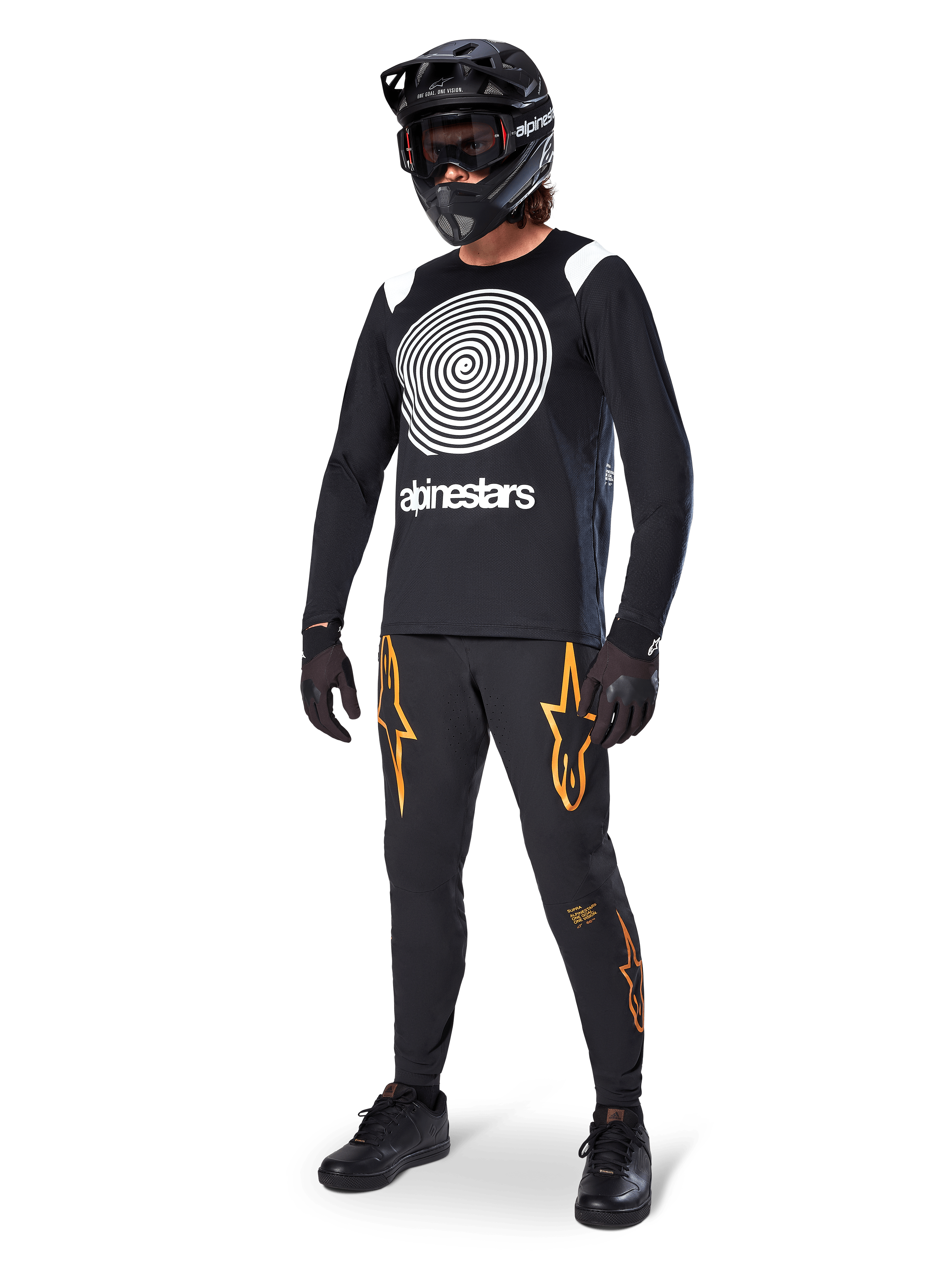 Pilota di MTB che indossa la maglia Alpinestars A-Supra Oscar a maniche lunghe nera, caratterizzata dalla grafica vintage a spirale Oscar bianca, pantaloni neri con loghi a stella arancioni, casco integrale nero con maschera e guanti neri, abbigliamento professionale da mountain bike