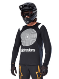 Alpinestars Maglia A-Supra Oscar a maniche lunghe, maglia da ciclismo MTB, nero e bianco, con un audace design a spirale bianca e logo Alpinestars sul petto, indossata con casco integrale nero e maschera, abbigliamento tecnico per mountain bike