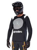 Alpinestars Maglia A-Supra Oscar a maniche lunghe, maglia da ciclismo MTB, nero e bianco, con un audace design a spirale bianca e logo Alpinestars sul petto, indossata con casco integrale nero e maschera, abbigliamento tecnico per mountain bike