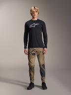 Maglia a maniche lunghe Alpinestars A-Dura Astar, nero, con un grande logo Astars bianco sul petto, indossata con pantaloni mimetici e scarpe nere, abbigliamento casual performante per mountain bike