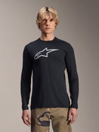 Alpinestars Maglia A-Dura Astar a maniche lunghe, nera con logo Astars argento sul petto, indossata da un modello con pantaloni mimetici, abbigliamento tecnico casual per mountain bike
