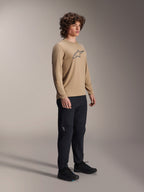 Alpinestars A-Dura Astar Long Sleeve Jersey, marrone chiaro, indossata da un modello con pantaloni e scarpe neri, con logo Astars grigio sul petto, abbigliamento tecnico casual per mountain bike