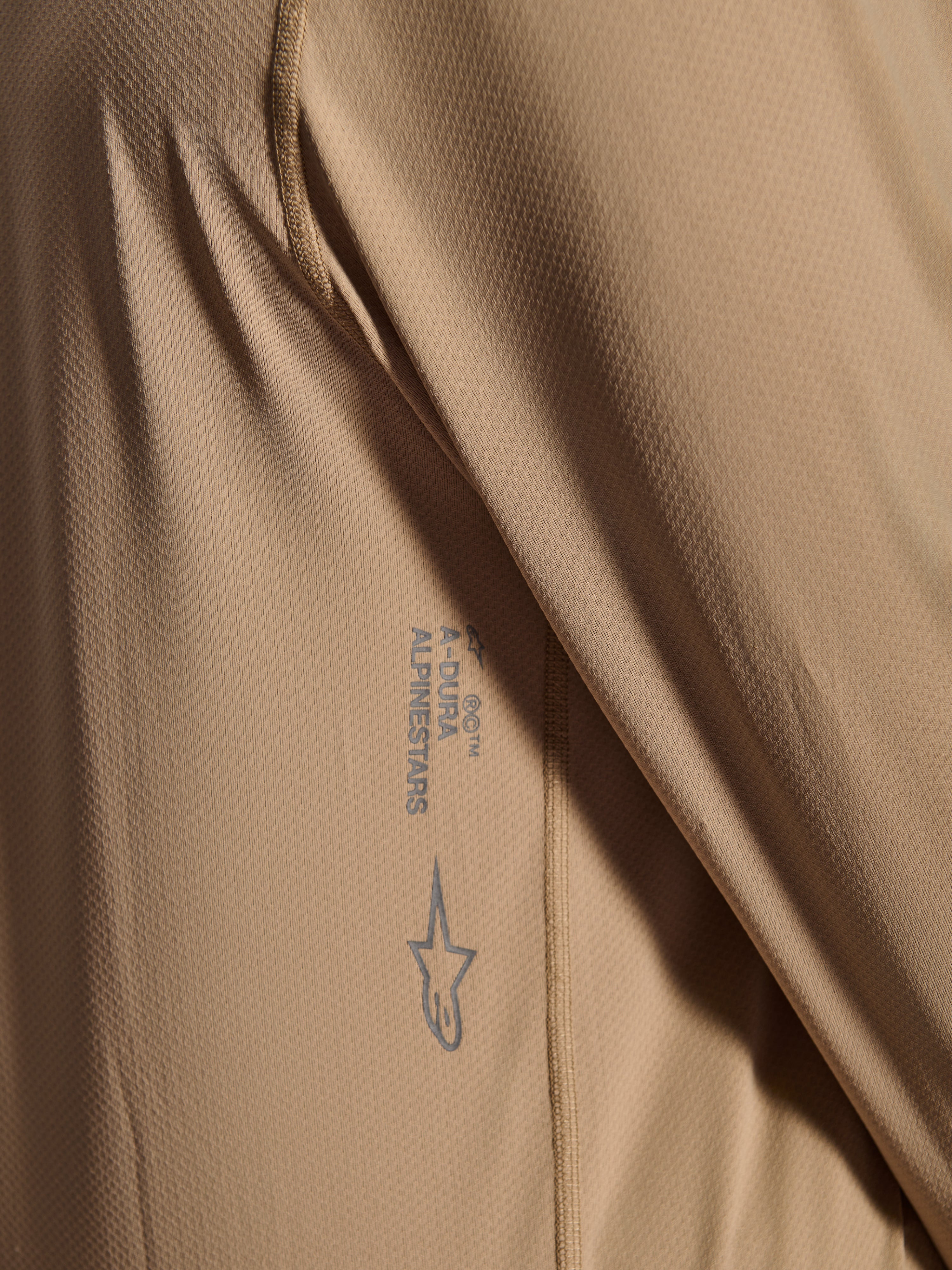 Alpinestars Maglia A-Dura Astar a maniche lunghe, maglia da ciclismo MTB, marrone, primo piano della trama del tessuto jacquard con logo Astars e scritta A-Dura, abbigliamento tecnico da mountain bike