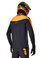 Alpinestars Maglia A-Supra Race - Maniche lunghe, nero e arancione, vista posteriore del pilota con casco e pantaloni da mountain bike coordinati, vestibilità performance con texture microperforata, abbigliamento professionale da gara MTB