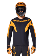 Rider MTB con maglia Alpinestars A-Supra Race - Maniche Lunghe, nera con grafiche arancioni e logo sul petto, indossata con casco integrale arancione coordinato, maschera nera e guanti arancioni, kit da gara coordinato per performance in mountain bike