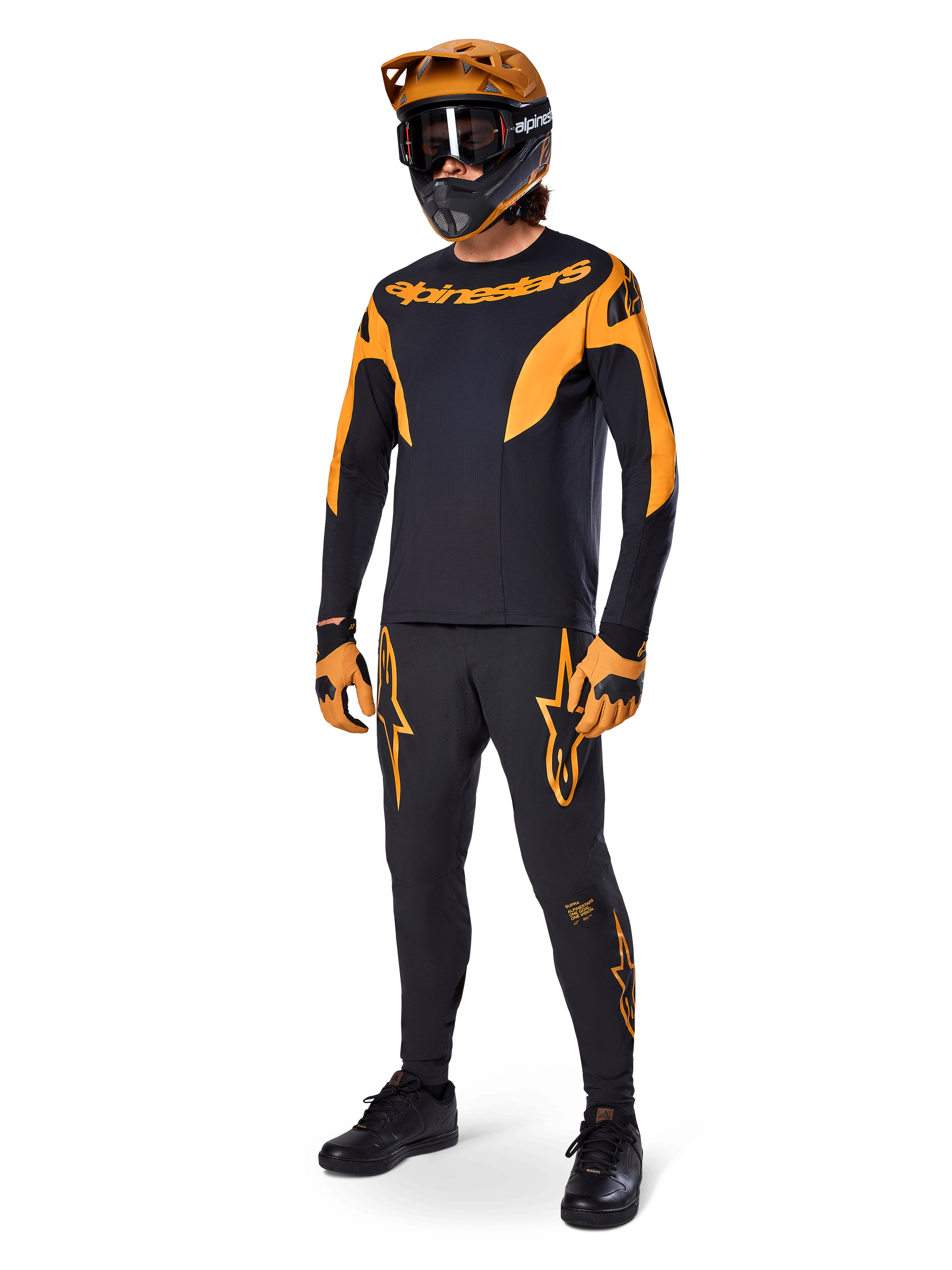Pilota MTB con abbigliamento completo da gara, maglia A-Supra Race nera con accenti arancioni, pantaloni neri coordinati con loghi Alpinestars arancioni, casco integrale arancione e nero con maschera, guanti arancioni e neri, outfit coordinato per gare di mountain bike