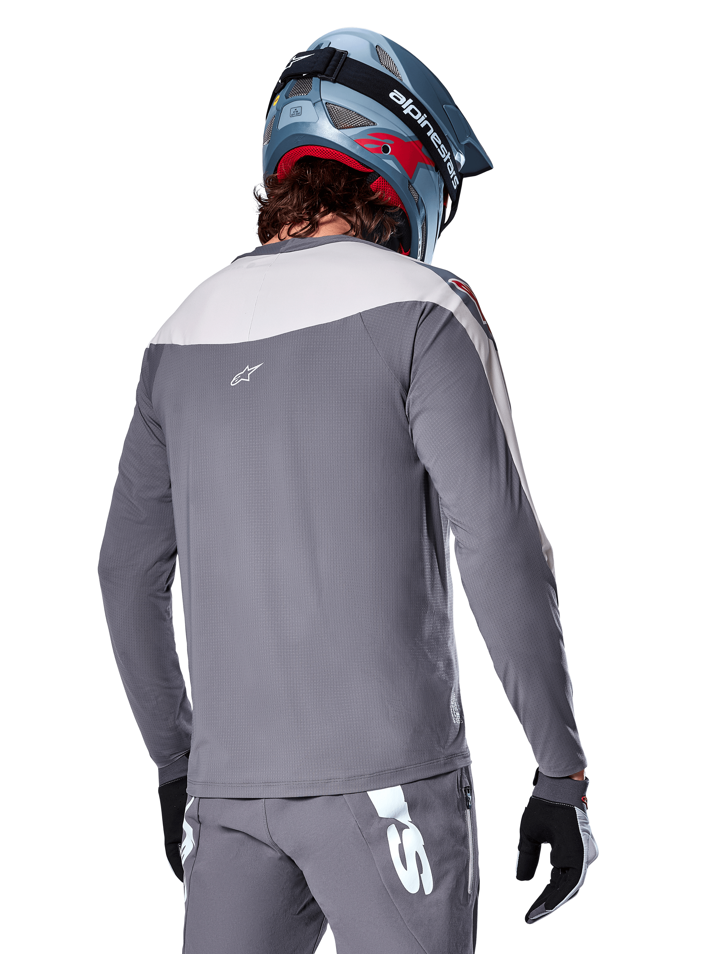 Alpinestars A-Supra Race Jersey, maglia MTB a maniche lunghe in grigio scuro e grigio chiaro, vista posteriore che mostra la vestibilità performance e il logo Astar, indossata con pantaloni grigi coordinati e un casco da mountain bike blu, progettata per il mountain bike fuoristrada.