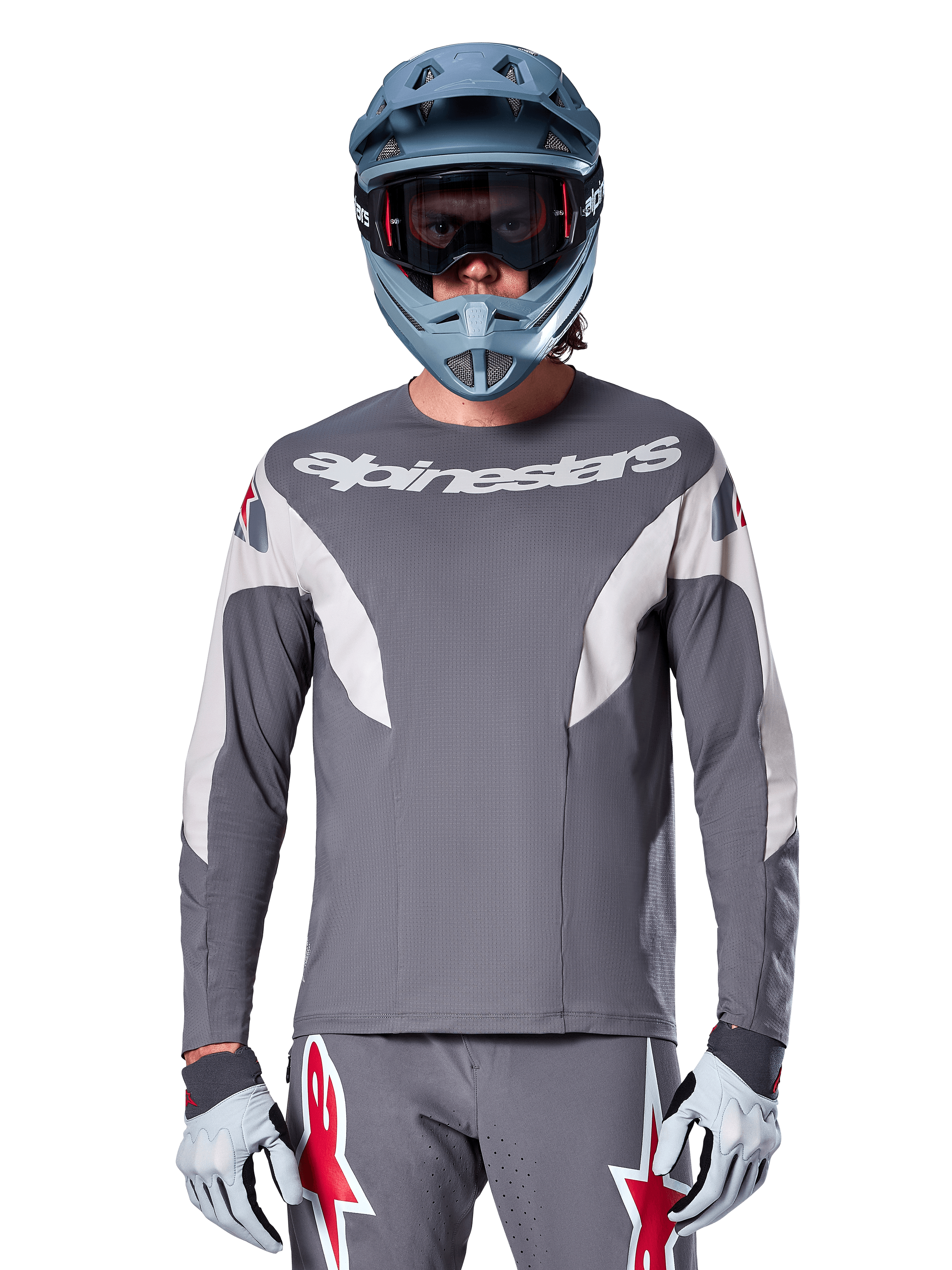 Ciclista MTB che indossa la maglia Alpinestars A-Supra Race - Manica Lunga in grigio scuro, maglia da ciclismo a maniche lunghe con logo Alpinestars bianco, abbinata a casco integrale grigio-azzurro, maschera e guanti da corsa grigi, equipaggiamento completo da gara per mountain bike per prestazioni off-road