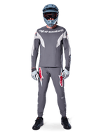 Rider con maglia Alpinestars A-Supra Race - Manica lunga in grigio scuro, coordinata con pantaloni grigi abbinati con vistosi loghi a stella rossi, casco grigio con maschera e guanti grigio chiaro, kit da gara MTB completo per il ciclismo fuoristrada ad alte prestazioni