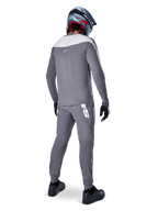 Alpinestars A-Supra Race Jersey, maglia MTB a maniche lunghe, grigio scuro con inserto sulle spalle grigio chiaro, vista posteriore indossata con pantaloni coordinati, casco integrale blu e rosso, guanti e scarpe neri, abbigliamento da ciclismo tecnico ispirato alle corse