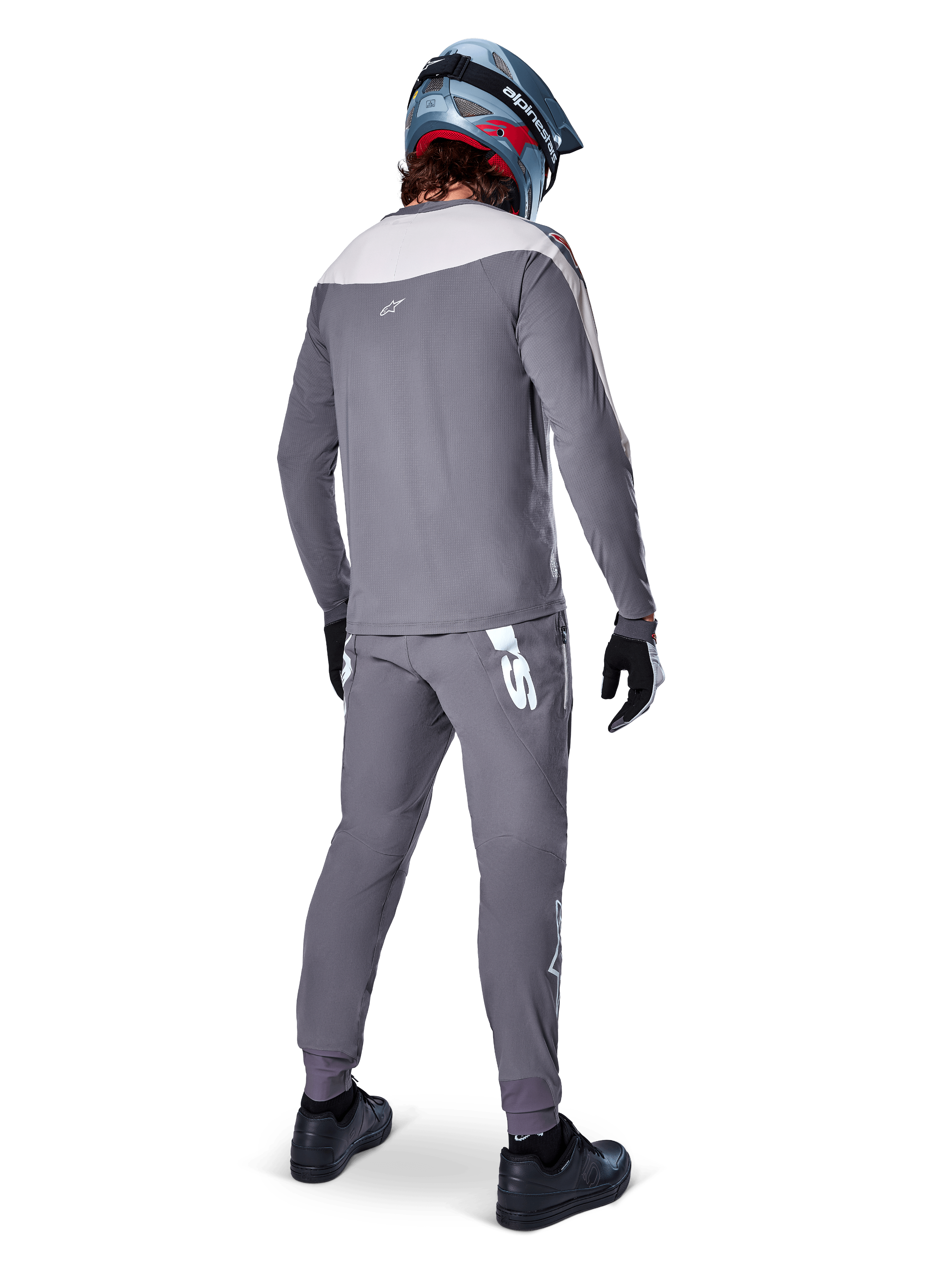 Alpinestars A-Supra Race Jersey, maglia MTB a maniche lunghe, grigio scuro con inserto sulle spalle grigio chiaro, vista posteriore indossata con pantaloni coordinati, casco integrale blu e rosso, guanti e scarpe neri, abbigliamento da ciclismo tecnico ispirato alle corse