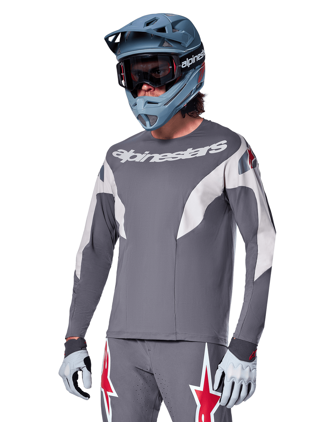 Alpinestars A-Supra Race Jersey a maniche lunghe, grigio scuro con dettagli bianchi e rossi, grafiche in stile racing, indossata con pantaloni grigi coordinati, casco integrale blu e guanti bianchi, equipaggiamento professionale per MTB e downhill
