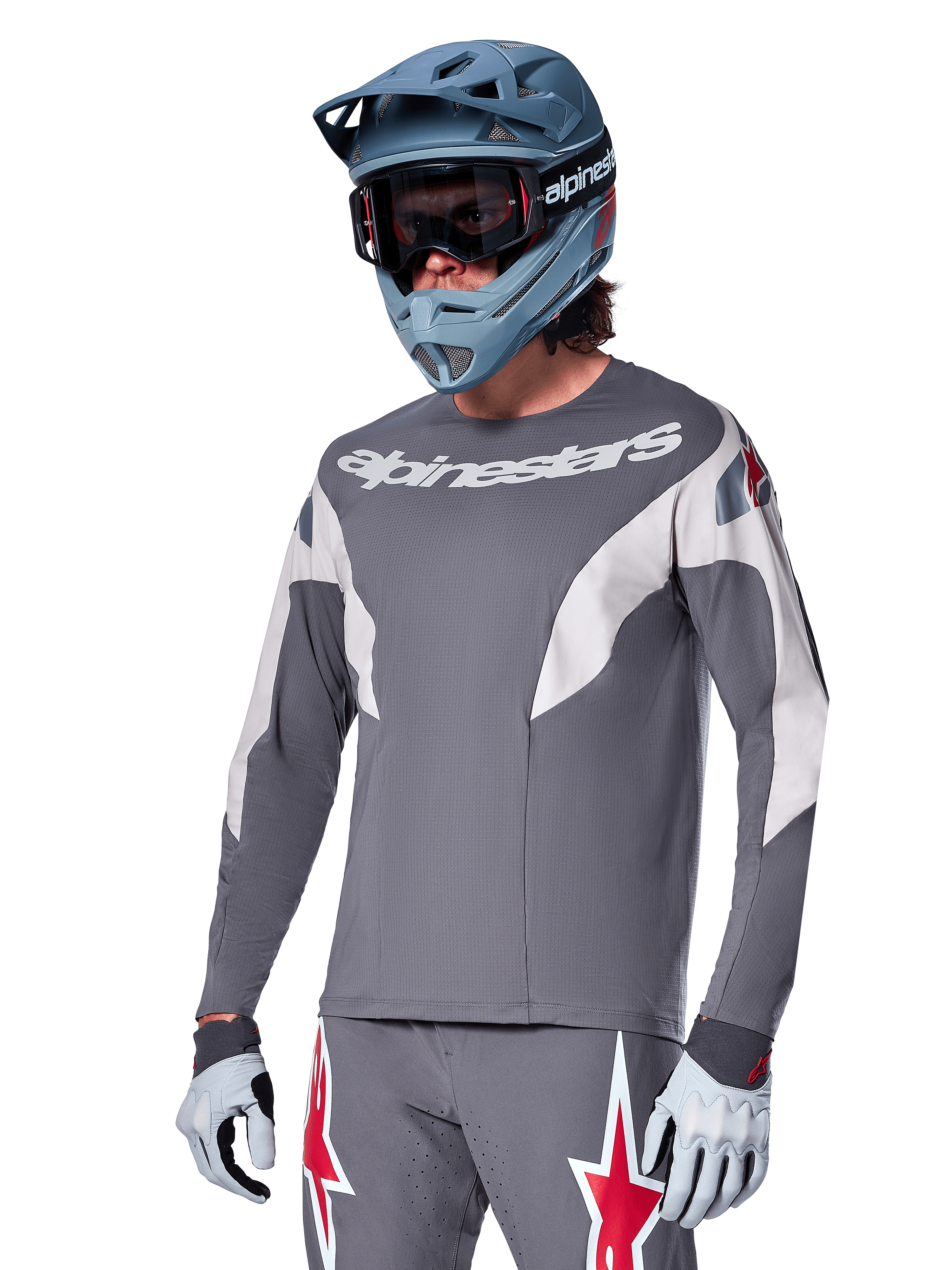 Alpinestars A-Supra Race Jersey a maniche lunghe, grigio scuro con dettagli bianchi e rossi, grafiche in stile racing, indossata con pantaloni grigi coordinati, casco integrale blu e guanti bianchi, equipaggiamento professionale per MTB e downhill