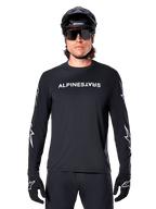 Alpinestars Maglia A-Dura Switch a maniche lunghe, maglia da MTB nera, scritta Alpinestars bianca sul petto e grafiche a stella sulle maniche, indossata con casco da mountain bike nero e occhiali tecnici, abbigliamento tecnico da trail