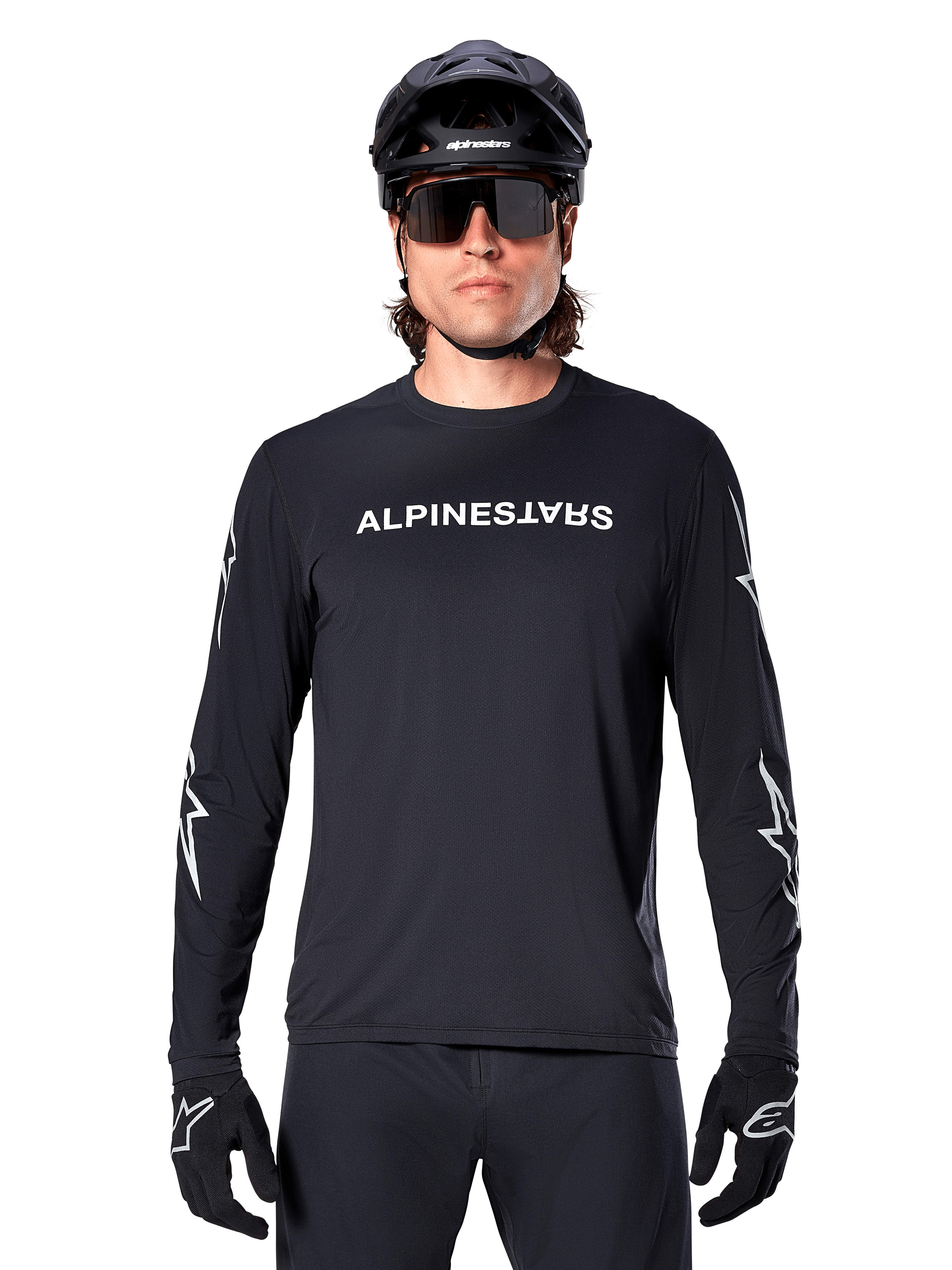Alpinestars Maglia A-Dura Switch a maniche lunghe, maglia da MTB nera, scritta Alpinestars bianca sul petto e grafiche a stella sulle maniche, indossata con casco da mountain bike nero e occhiali tecnici, abbigliamento tecnico da trail