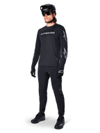 Maglia a maniche lunghe Alpinestars A-Dura Switch, nero, maglia da mountain bike indossata con pantaloni neri, casco e guanti, con logo wordmark bianco sul petto e loghi a stella sulle maniche, equipaggiamento MTB coordinato per la guida fuoristrada