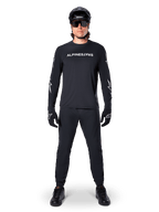 Maglia Alpinestars A-Dura Switch a maniche lunghe, nero, indossata da un ciclista di mountain bike con pantaloni e casco neri coordinati, con logo wordmark bianco sul petto, abbigliamento tecnico per ciclismo fuoristrada