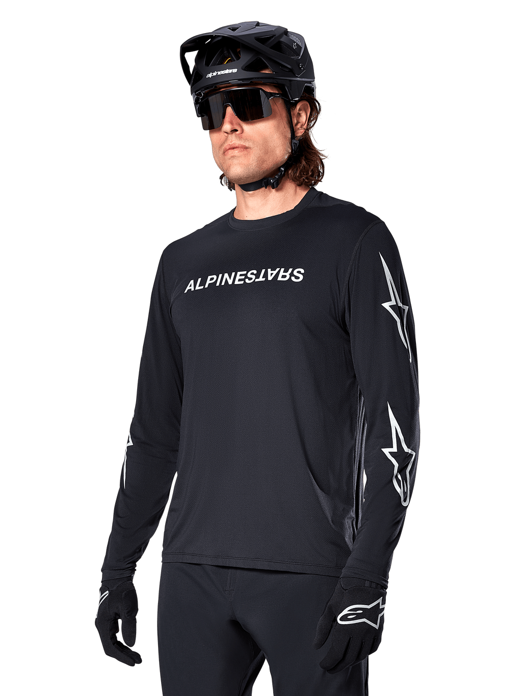 Ciclista uomo che indossa la maglia a maniche lunghe Alpinestars A-Dura Switch, nero con scritta bianca e loghi a stella sulle maniche, abbinata a casco MTB nero e occhiali da sole, abbigliamento da ciclismo ad alte prestazioni per la guida fuoristrada