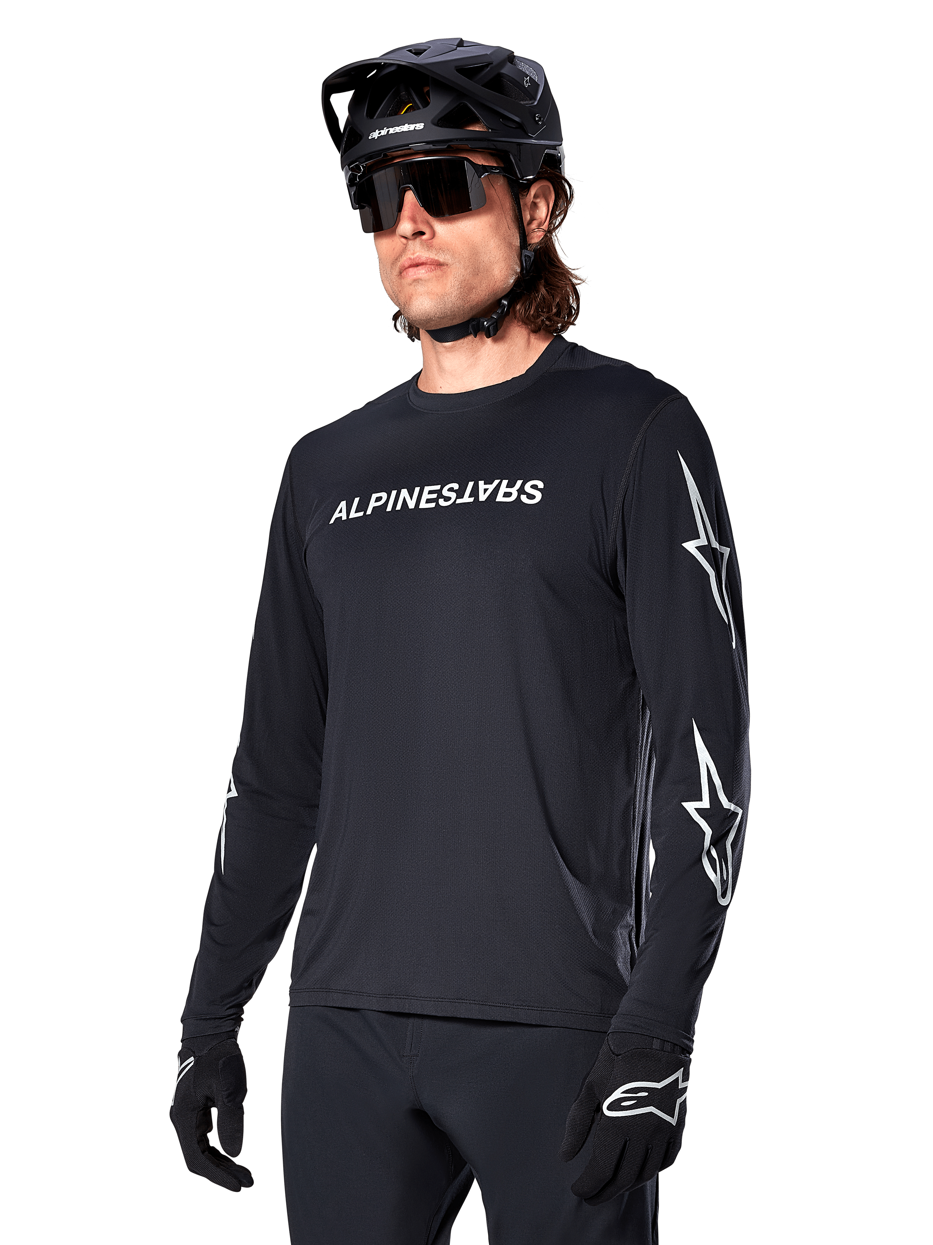 Ciclista uomo che indossa la maglia a maniche lunghe Alpinestars A-Dura Switch, nero con scritta bianca e loghi a stella sulle maniche, abbinata a casco MTB nero e occhiali da sole, abbigliamento da ciclismo ad alte prestazioni per la guida fuoristrada