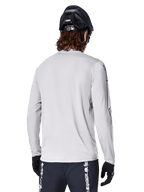 Alpinestars Maglia A-Dura Switch Long Sleeve, Grigio Chiaro, vista posteriore di un mountain biker con casco da MTB nero e guanti, con coda posteriore allungata e tessuto jacquard, abbigliamento tecnico da ciclismo