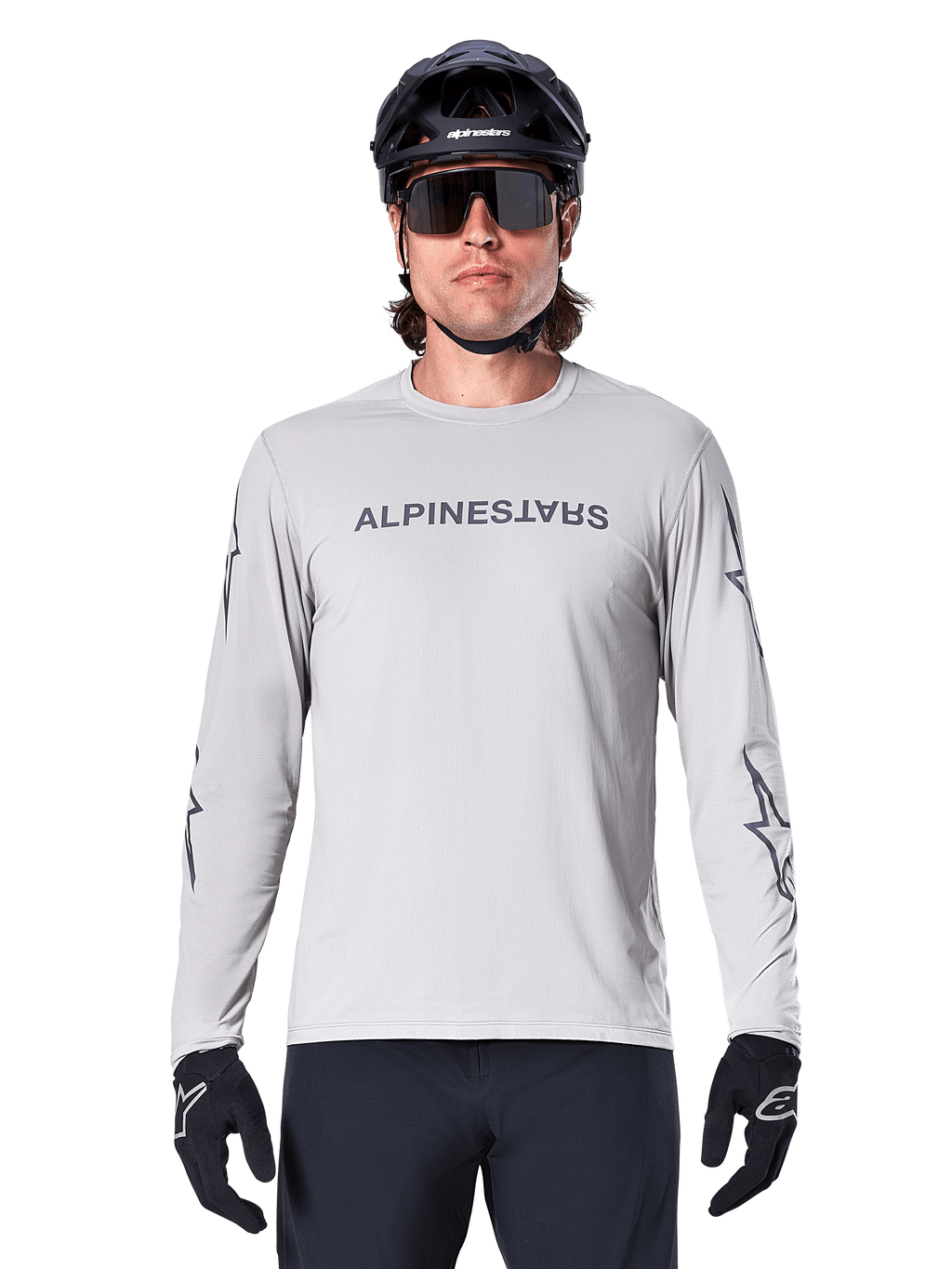 Maglia Alpinestars A-Dura Switch a maniche lunghe, grigio chiaro, con scritta sul petto e loghi a stella sulle maniche in grigio scuro, indossata da un ciclista con casco da MTB e guanti neri, abbigliamento tecnico da ciclismo per trail