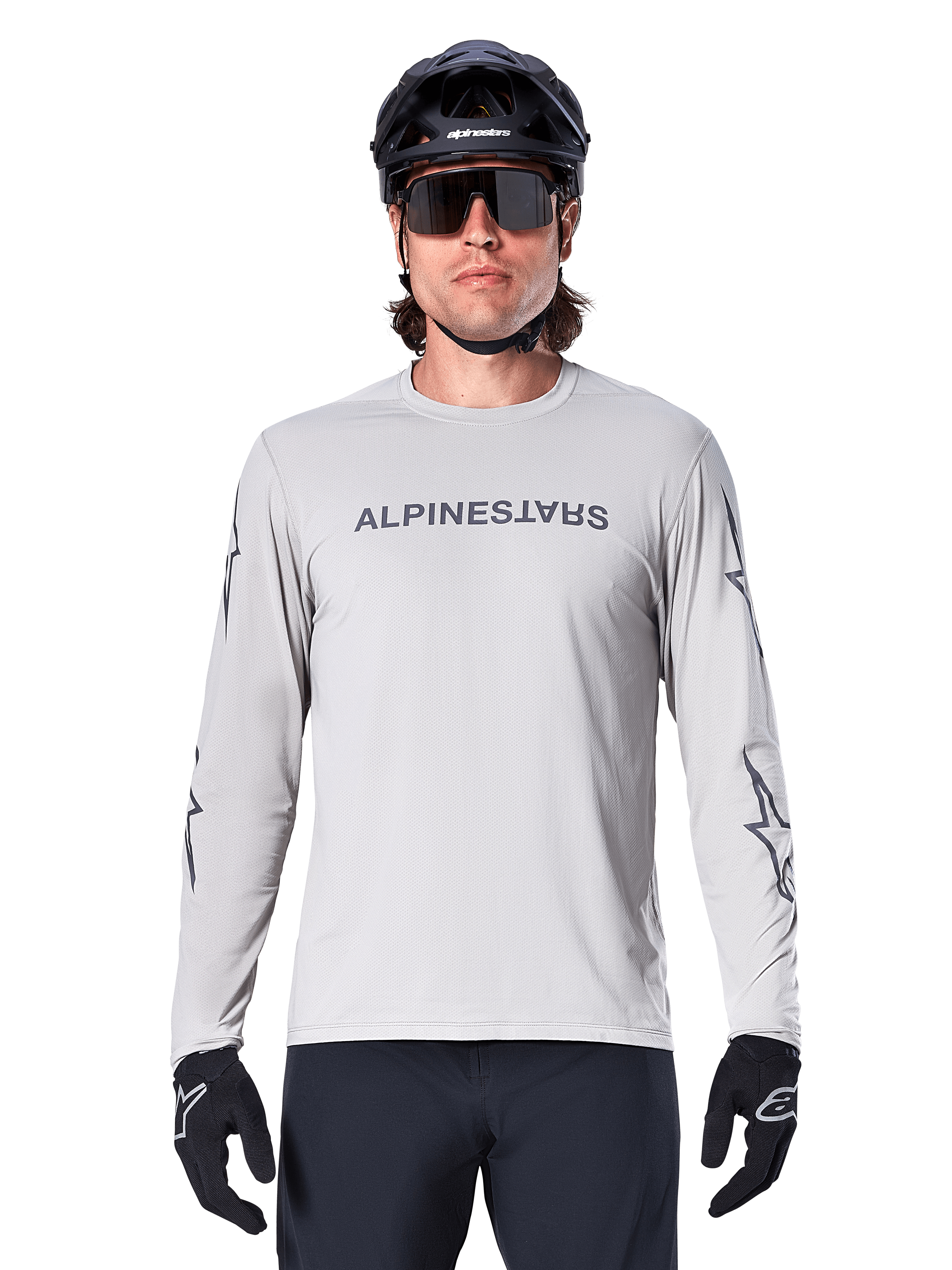 Maglia Alpinestars A-Dura Switch a maniche lunghe, grigio chiaro, con scritta sul petto e loghi a stella sulle maniche in grigio scuro, indossata da un ciclista con casco da MTB e guanti neri, abbigliamento tecnico da ciclismo per trail